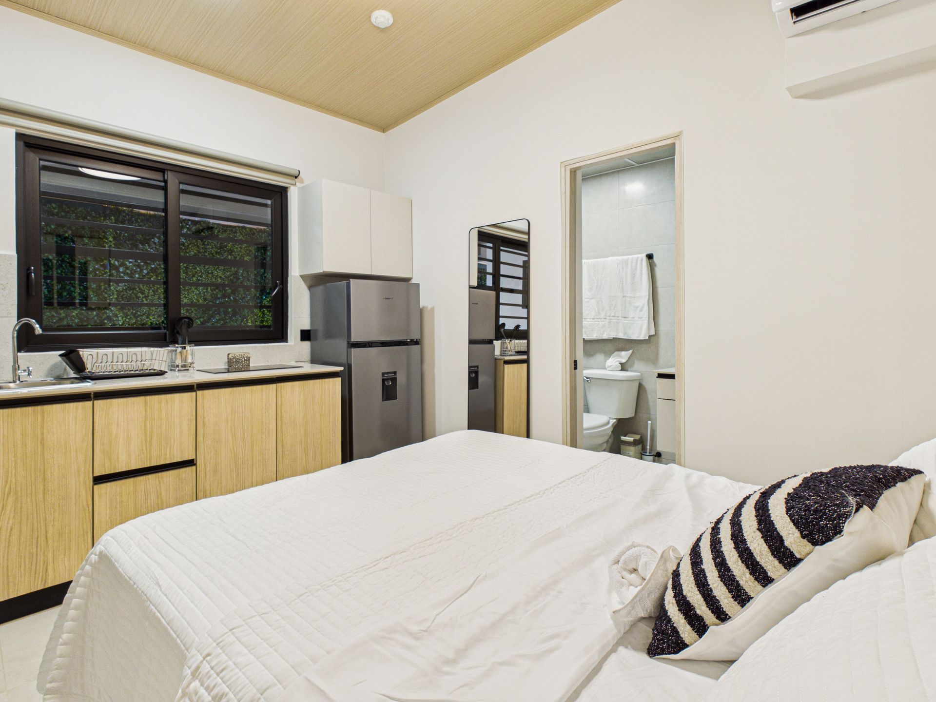 Un pequeño y moderno estudio que cuenta con una cama en primer plano, una zona de cocina con armarios de madera y un baño. en Bethania, Ciudad de Panamá. Fotografía de real estate