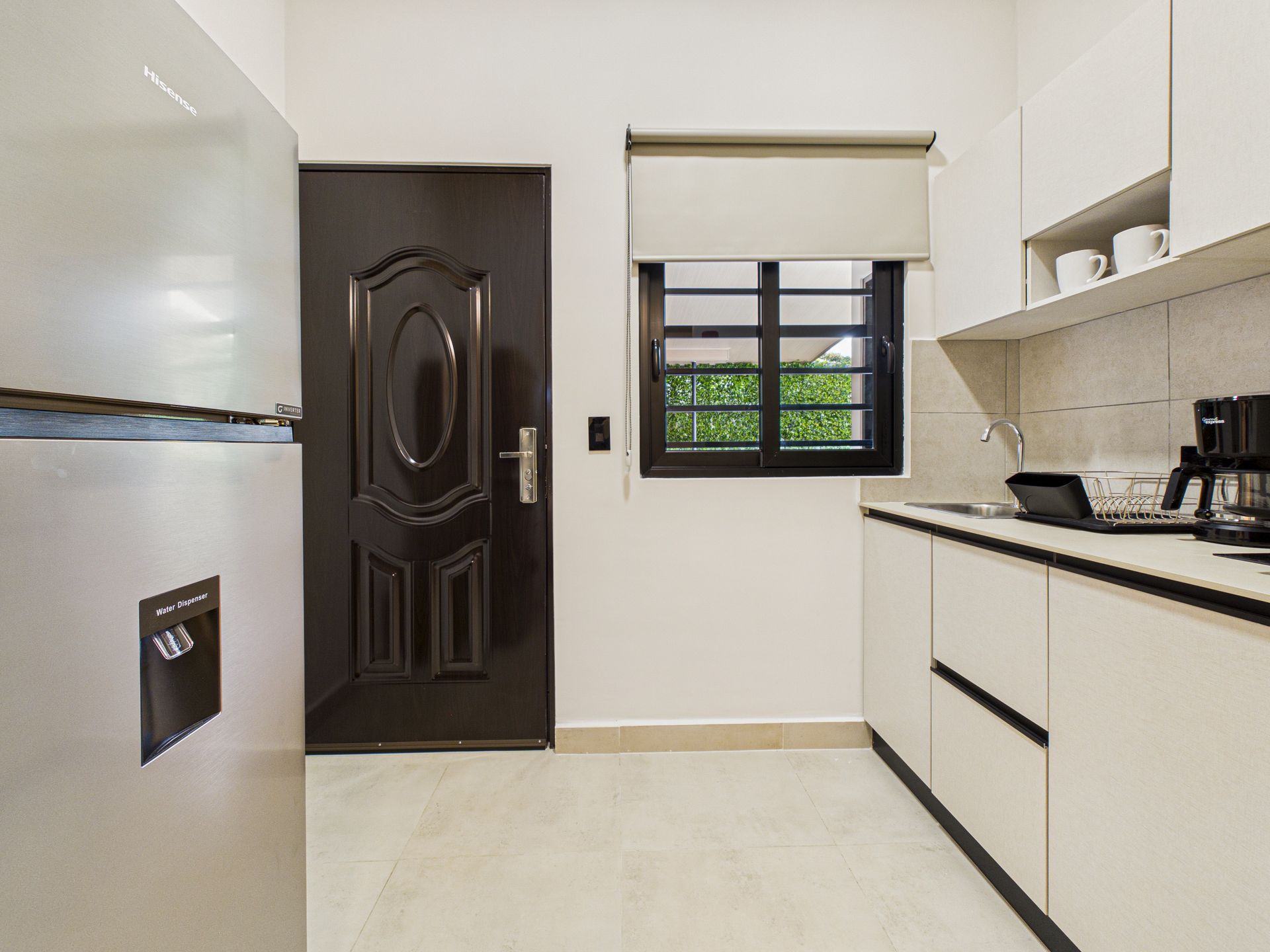 Una cocina moderna con armarios blancos, un frigorífico de acero inoxidable, una puerta negra y una ventana con persiana enrollable. en Bethania, Ciudad de Panamá. Fotografía de real estate