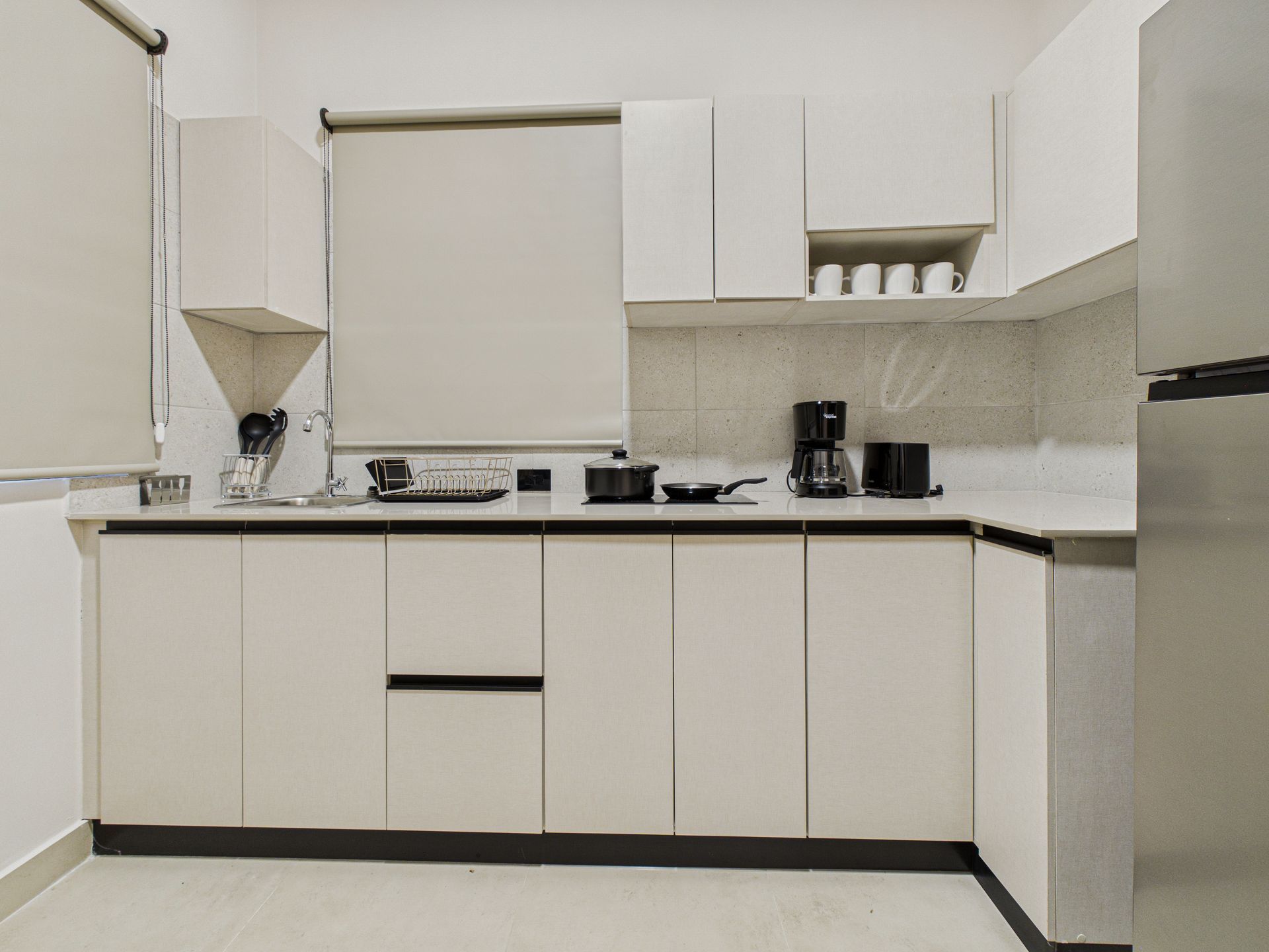 Cocina moderna con armarios blancos, encimeras claras, electrodomésticos de acero inoxidable y una ventana con una persiana enrollable de color neutro. en Bethania, Ciudad de Panamá. Fotografía de real estate