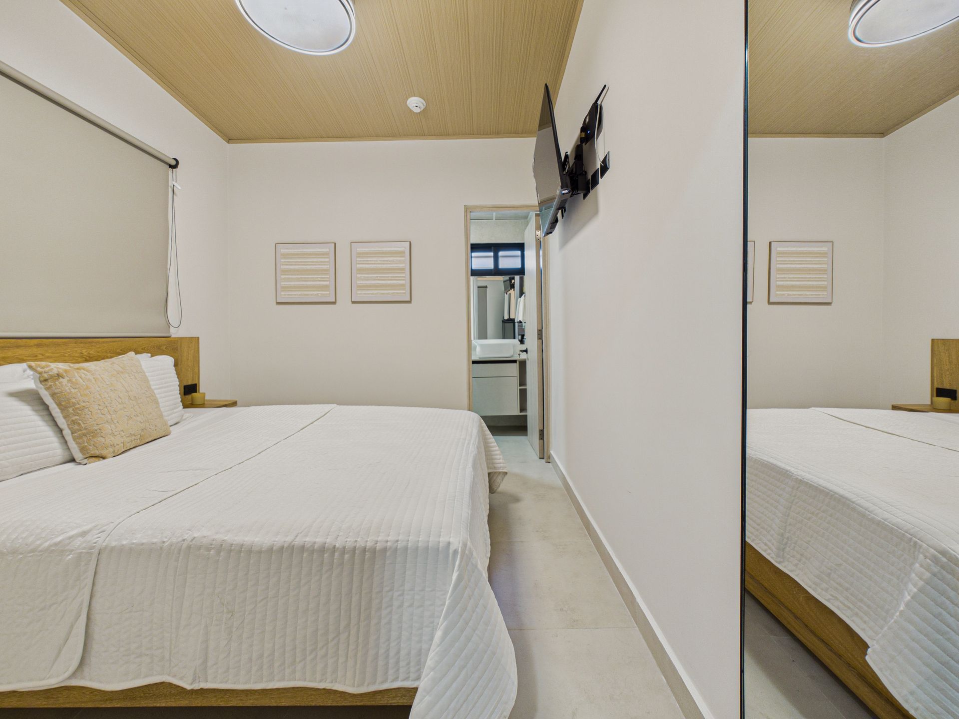 Una habitación de hotel con cama de matrimonio, techo con textura, armario con espejo y una puerta que da a un baño luminoso. 