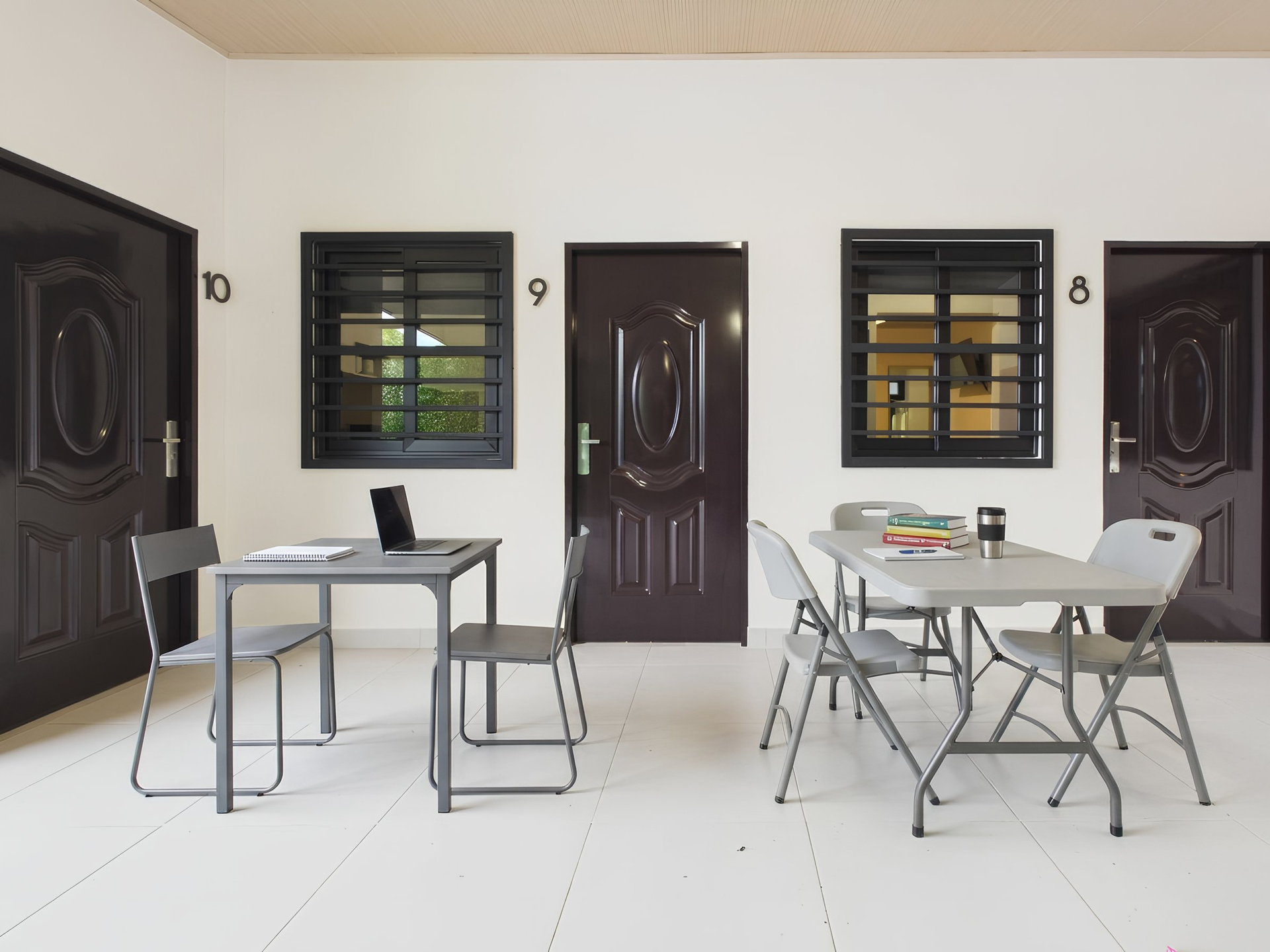 Dos mesas con sillas dispuestas en un patio blanco frente a tres puertas de color marrón oscuro numeradas 10, 9 y 8. en Bethania, Ciudad de Panamá. Fotografía de real estate