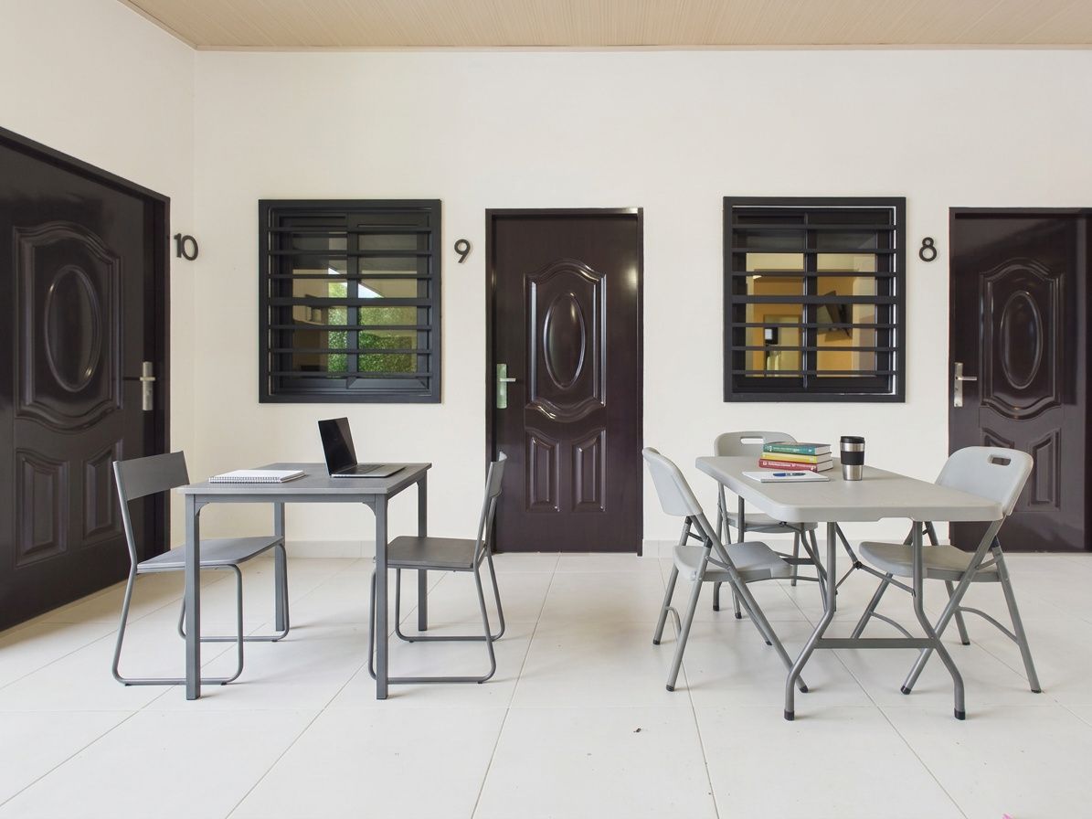 Dos mesas con sillas plegables grises están dispuestas frente a un edificio con tres puertas y ventanas numeradas de color marrón oscuro.en Bethania, Ciudad de Panamá. Fotografía de real estate