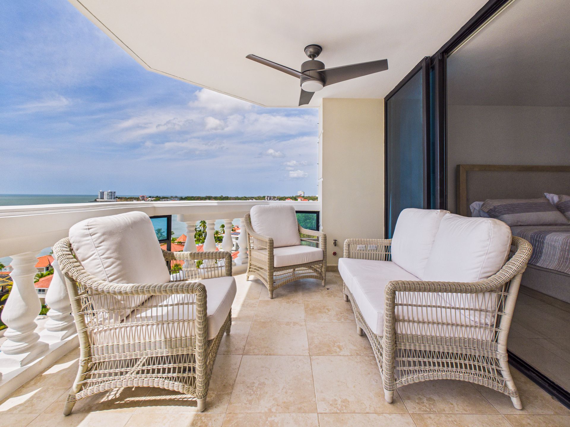 Balcony with wicker lounge chairs and sea view under a ceiling fan