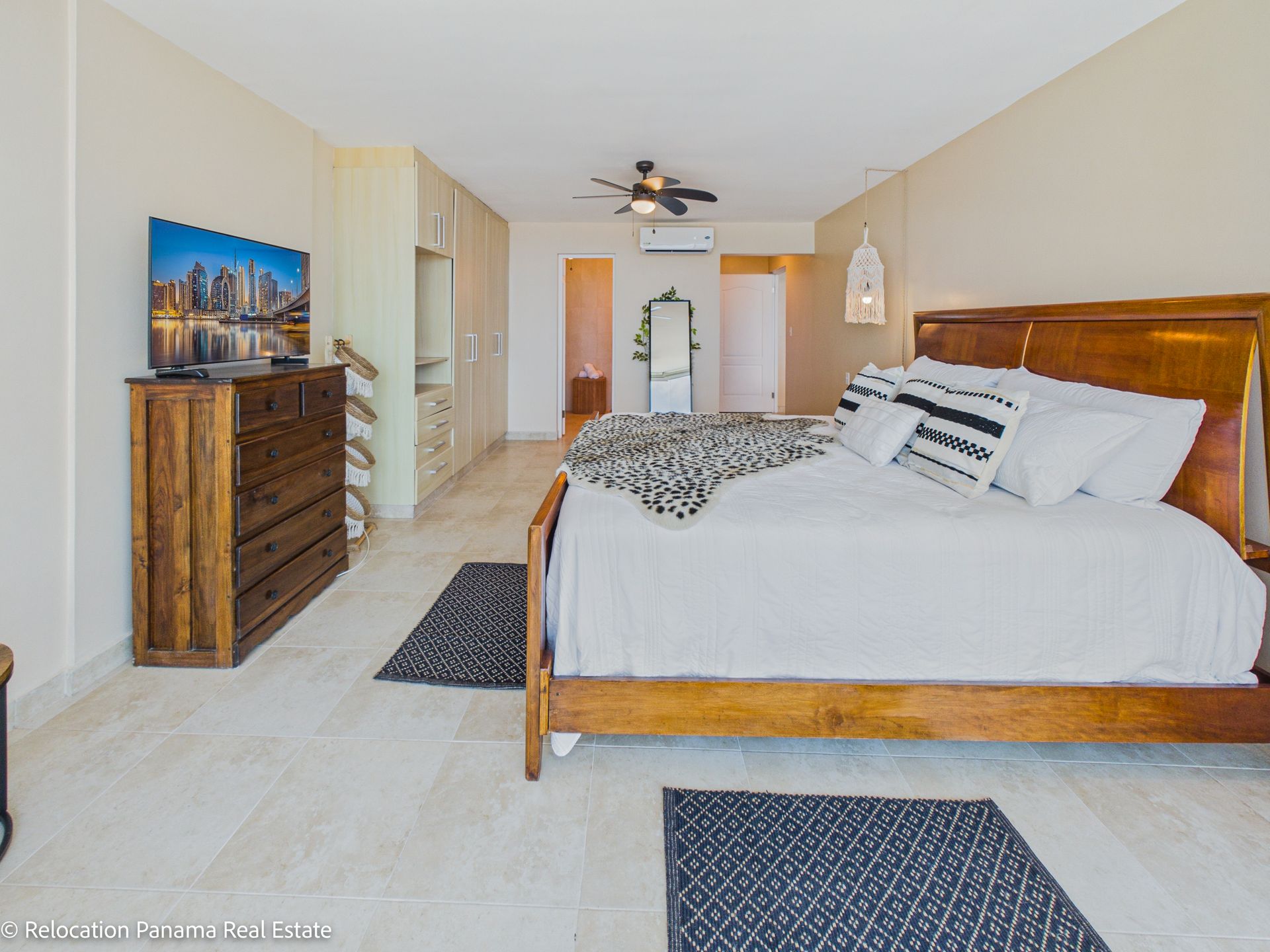 Un dormitorio con una cama grande de madera, una cómoda de madera, un televisor y suelos de baldosas de color claro.