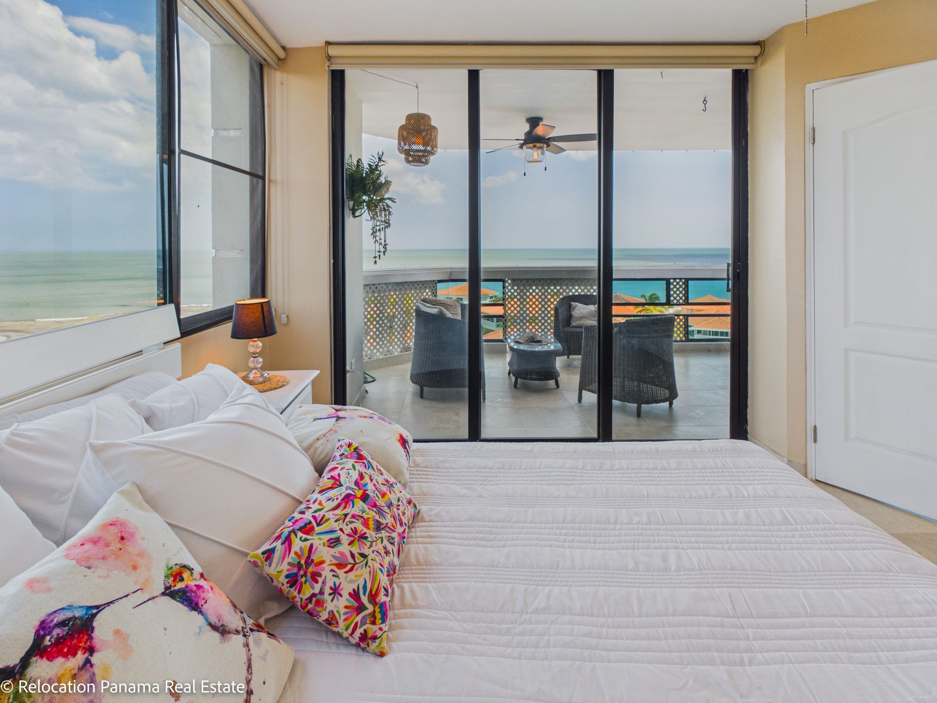 Un dormitorio con una cama con almohadas estampadas, con vistas a un balcón con muebles de exterior y vistas al mar.