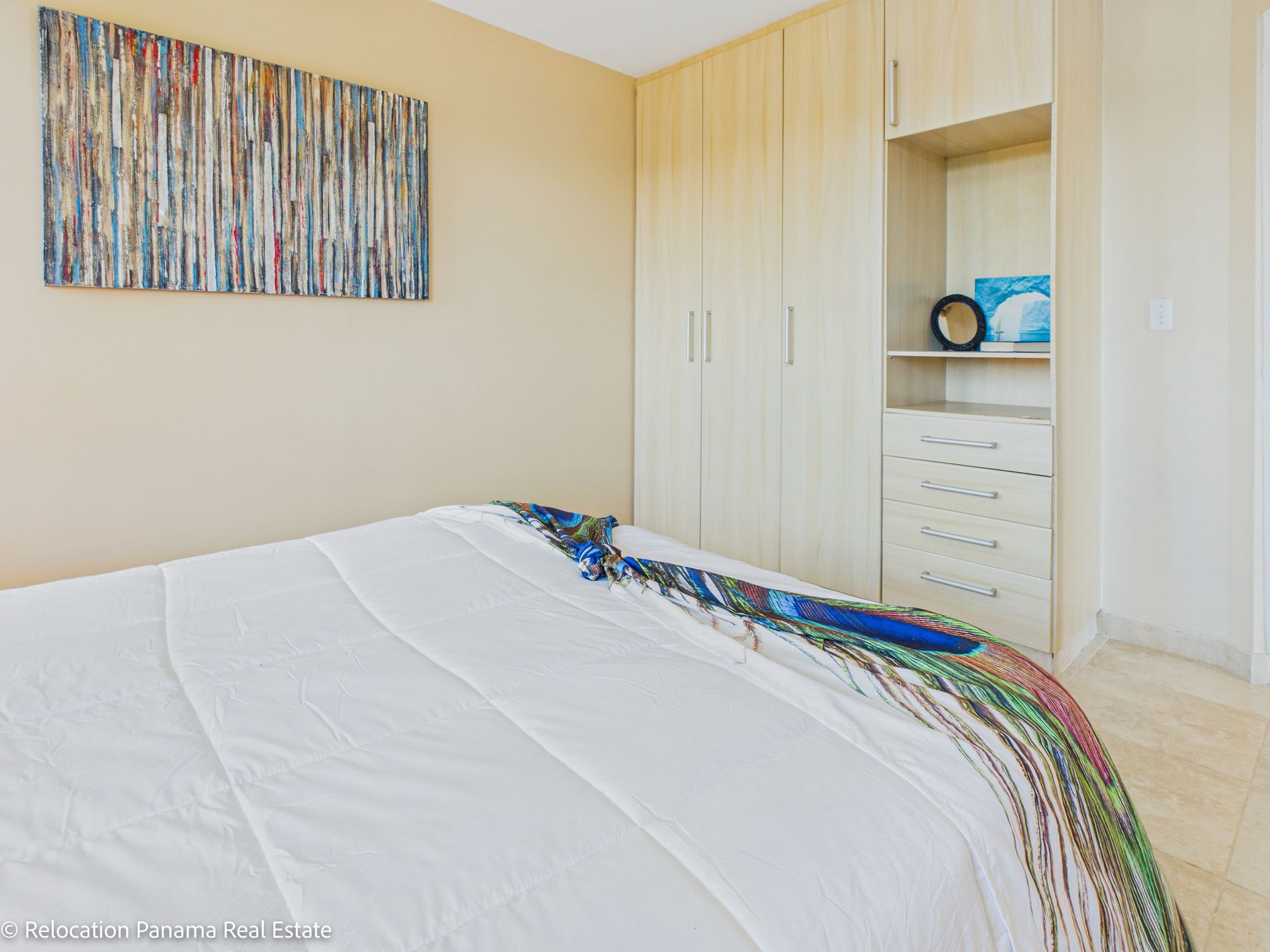 En un dormitorio de tonos neutros, una cama con una manta estampada se encuentra junto a un armario de madera clara con estantes y cajones.