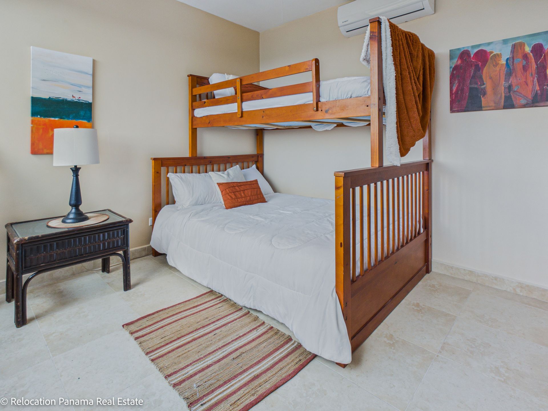 Una litera de madera con una cama inferior de tamaño estándar y una cama superior individual, con una mesita de noche, una lámpara y cuadros en la pared, en un dormitorio.