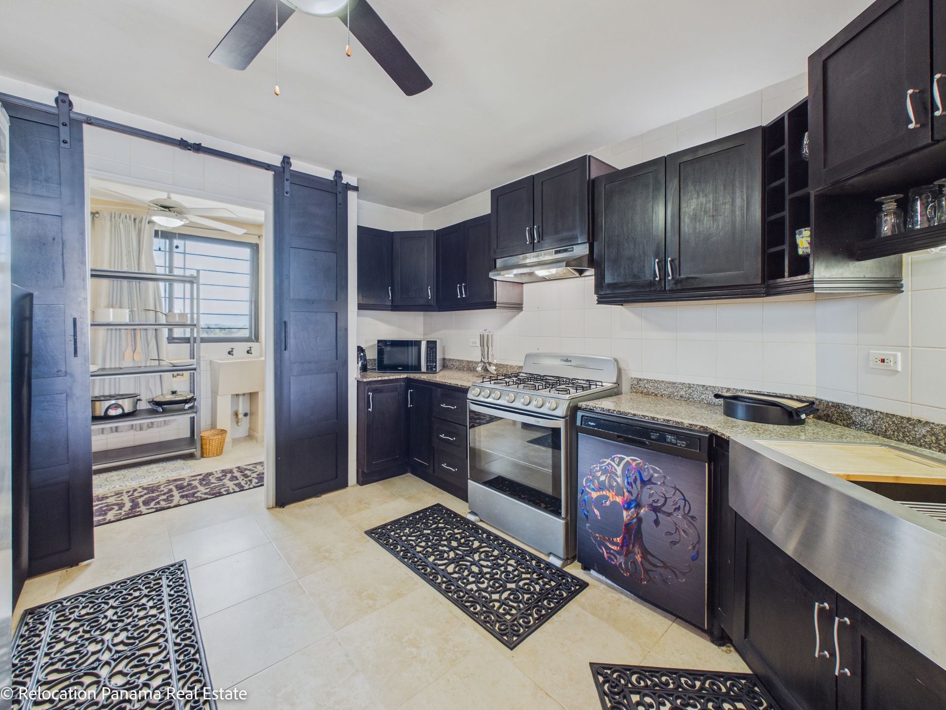 Una cocina con armarios de madera oscura, electrodomésticos de acero inoxidable, encimeras moteadas y suelos de baldosas con alfombras.