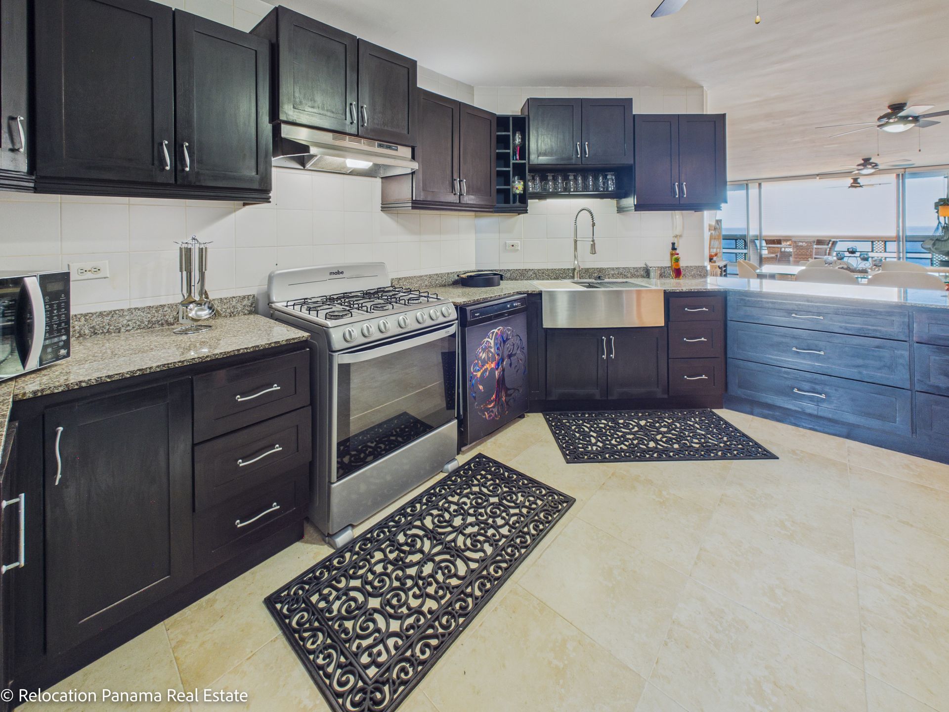 Cocina moderna con gabinetes oscuros, encimeras de granito, estufa de acero inoxidable, fregadero estilo granja y piso de baldosas.