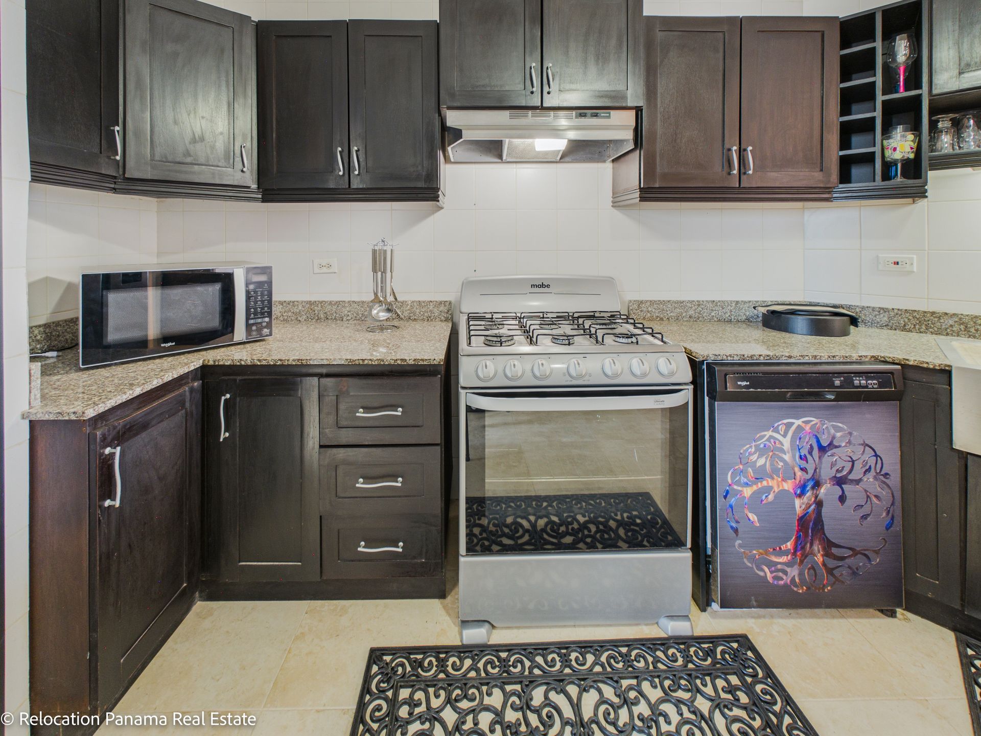 Una cocina con armarios de madera oscura, encimeras de granito, microondas, cocina de acero inoxidable y lavavajillas con un dibujo de un árbol.