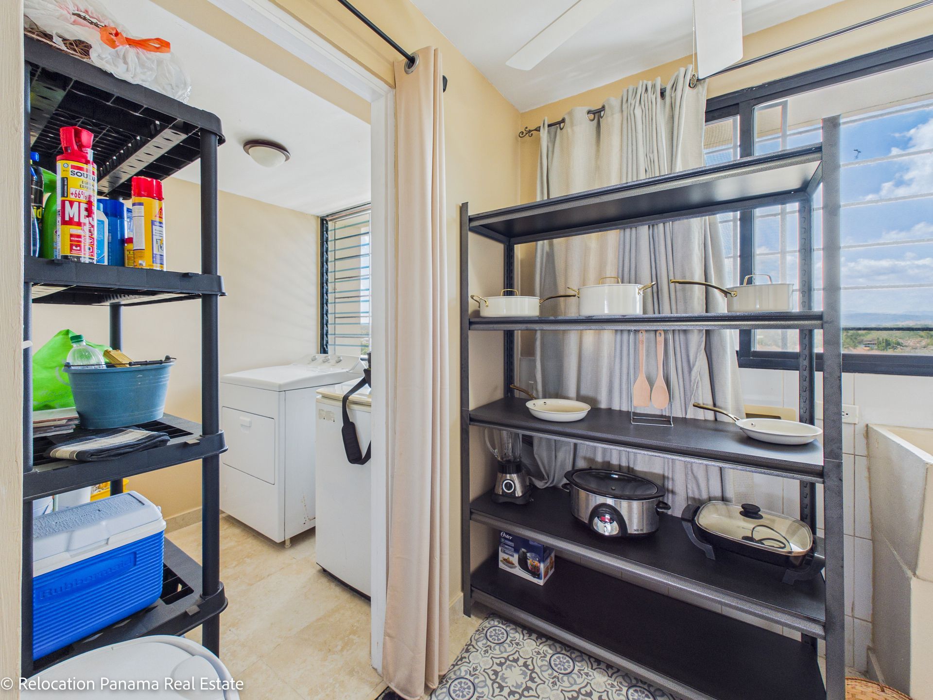 Dos estantes negros en una habitación; el de la izquierda contiene productos de limpieza y una nevera portátil, y el de la derecha, utensilios de cocina.