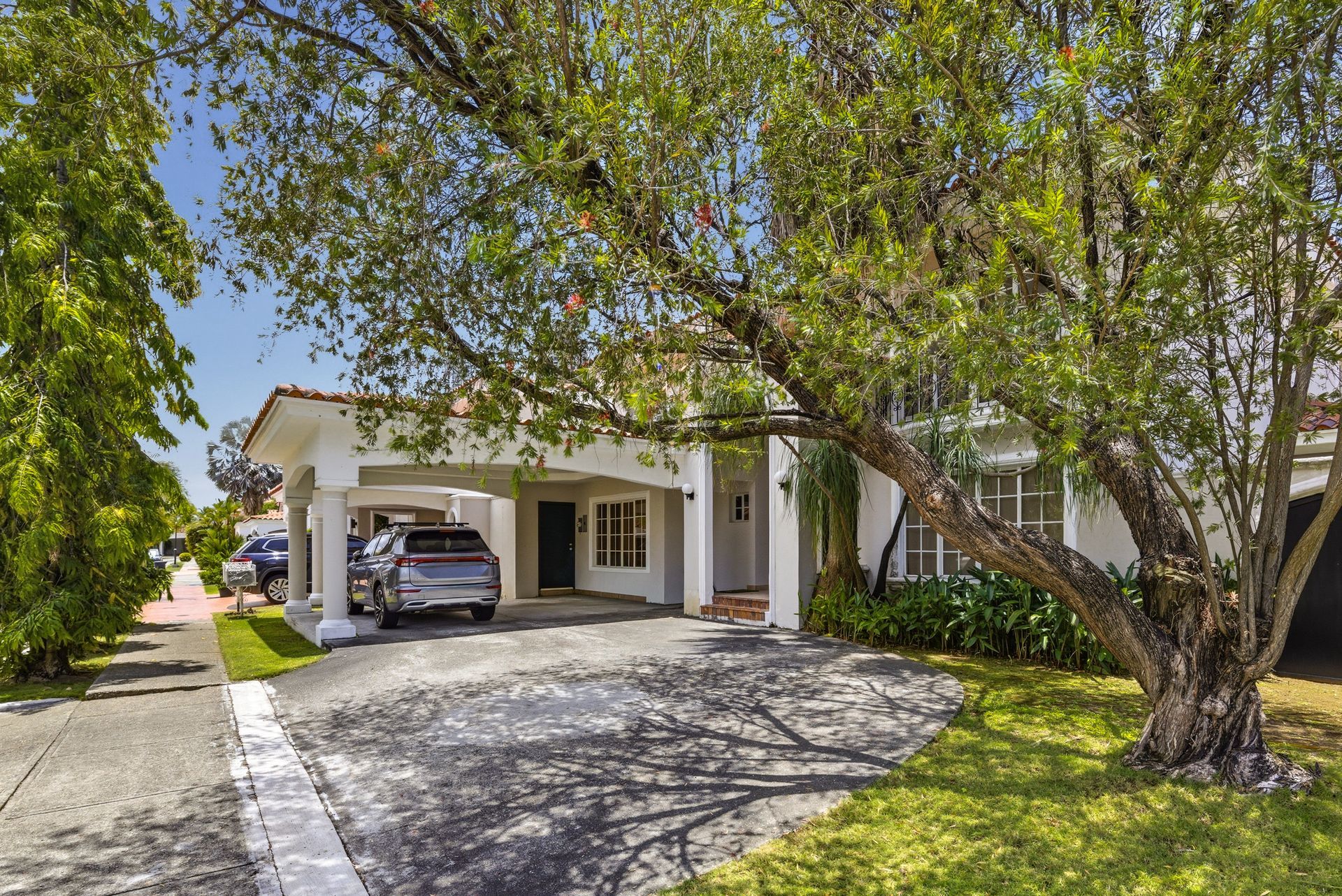 Suburban house with a car in the driveway, shaded by large trees and a front porch