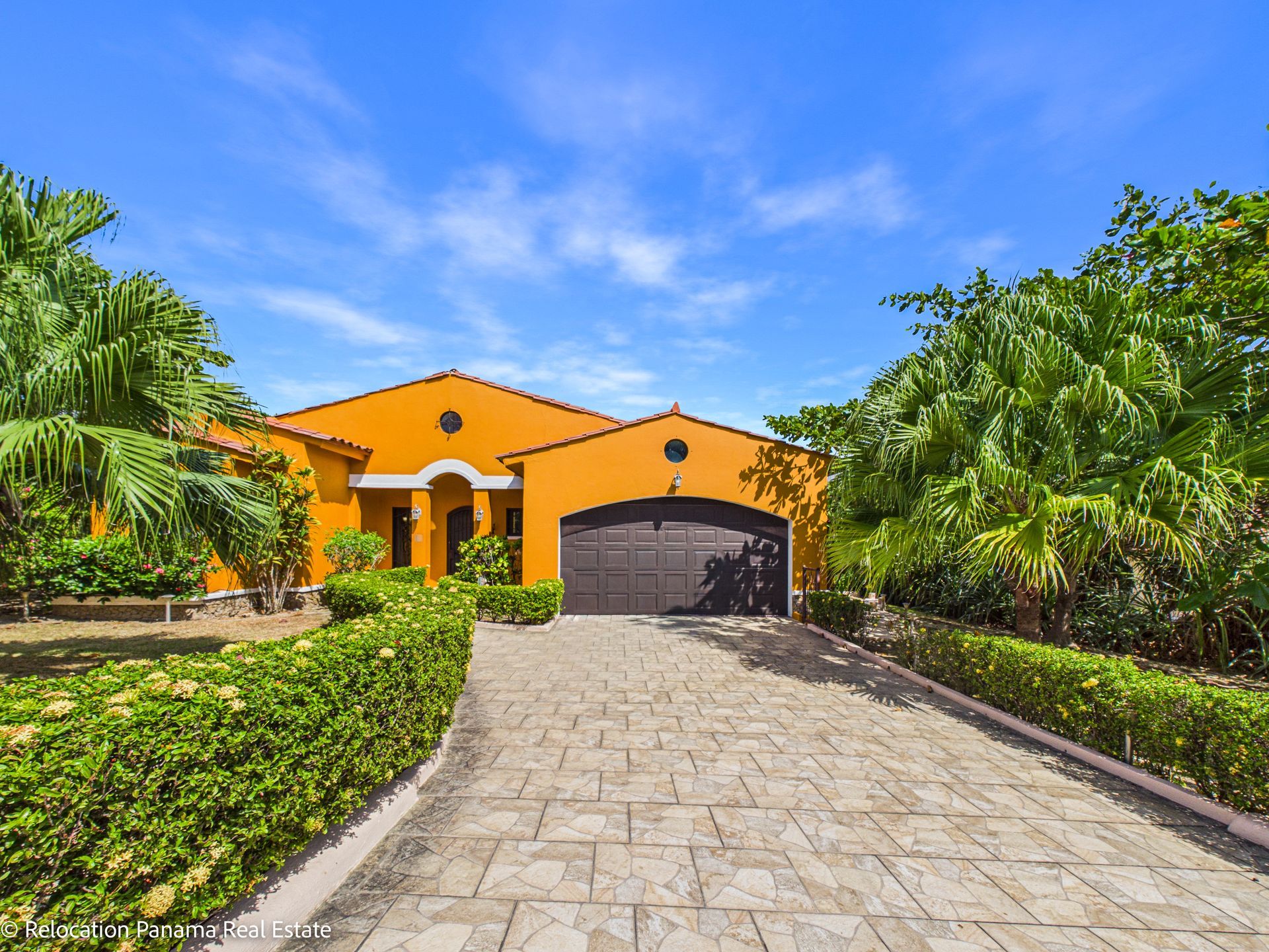 Una casa de una sola planta, de color naranja brillante, con entrada pavimentada, puerta de garaje de color marrón oscuro y un exuberante jardín verde.
