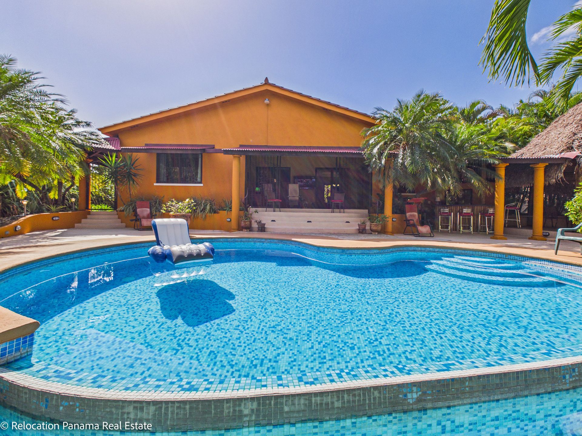Una casa de color naranja brillante con un patio y exuberante vegetación tropical que rodea una piscina azul con forma de riñón.