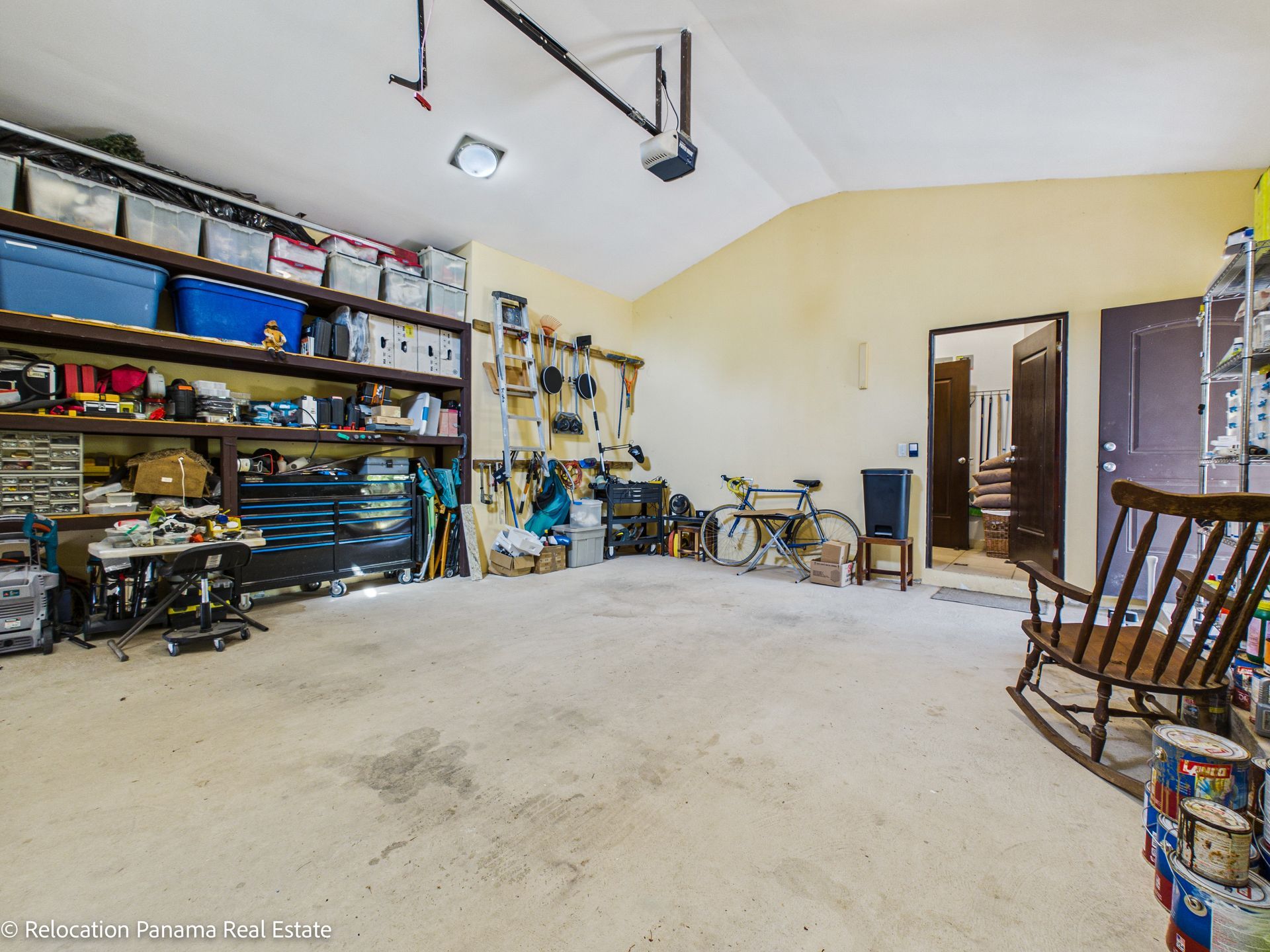 Un garaje espacioso con paredes de color beige, amplios estantes de almacenamiento, un banco de trabajo, una bicicleta y una mecedora de madera.