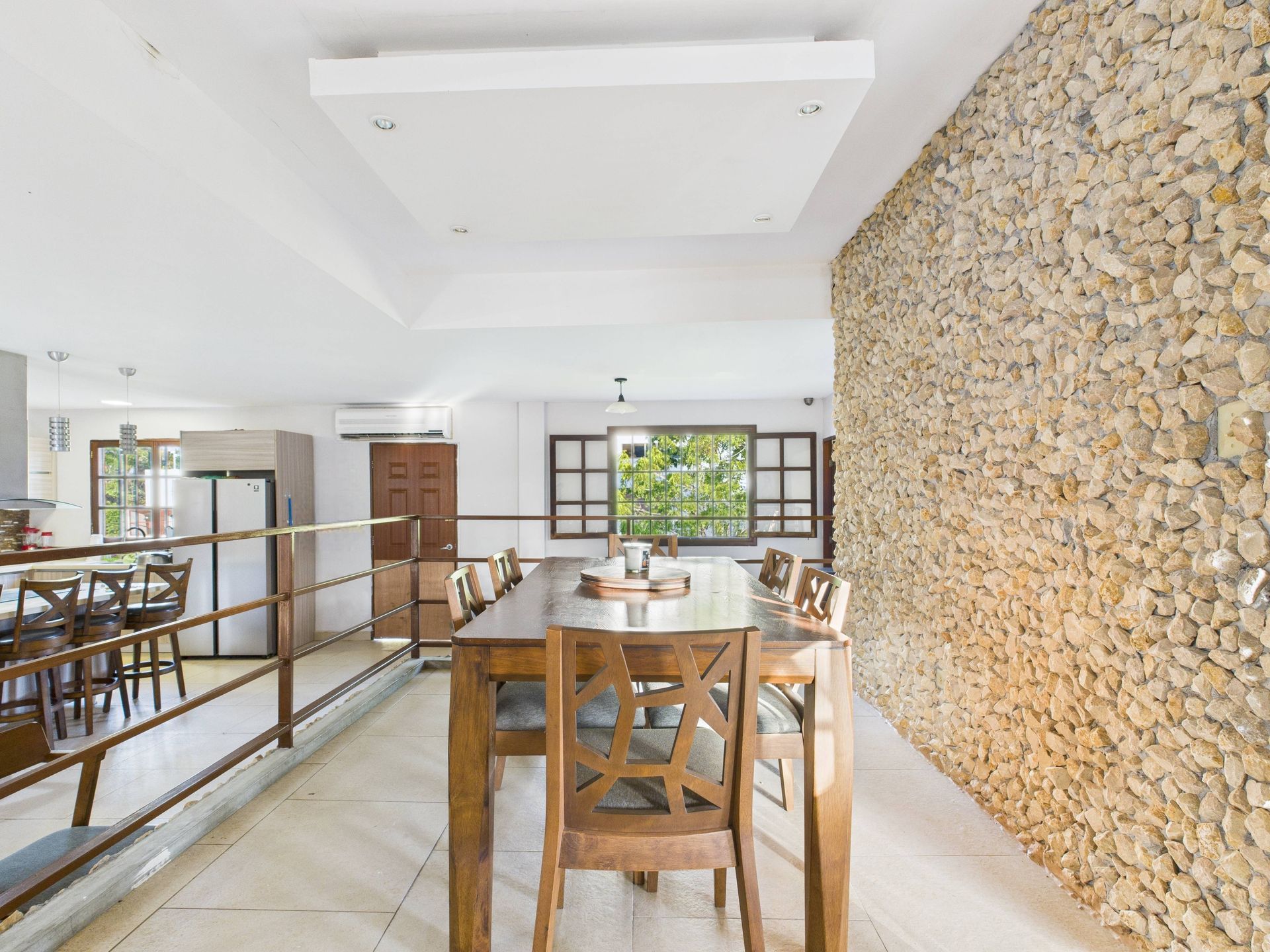 Comedor con mesa y sillas de madera, pared de piedra y ventanal con vista a zona verde.