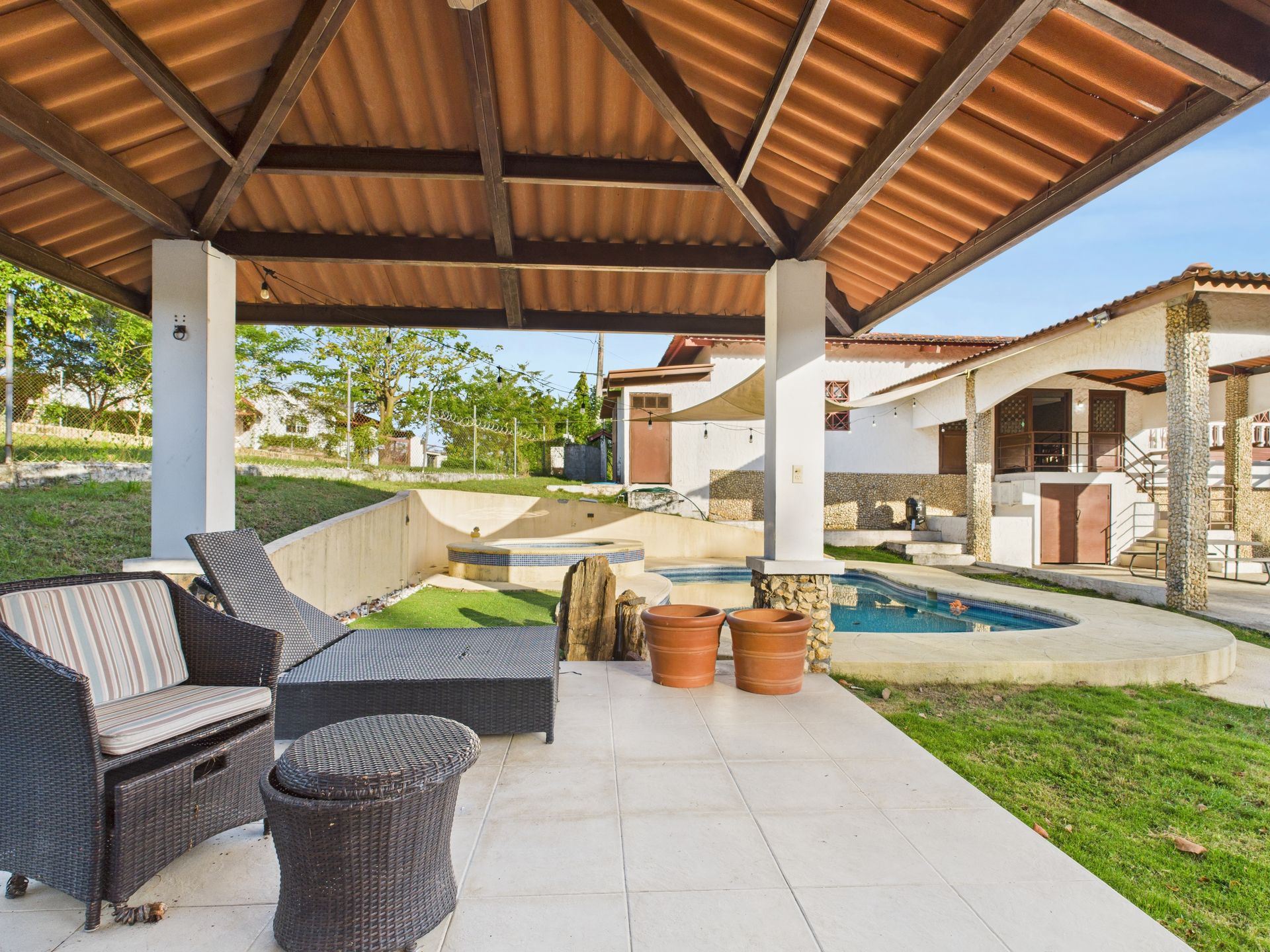 Patio con muebles de mimbre, pequeña piscina y una casita bajo una pérgola de madera.