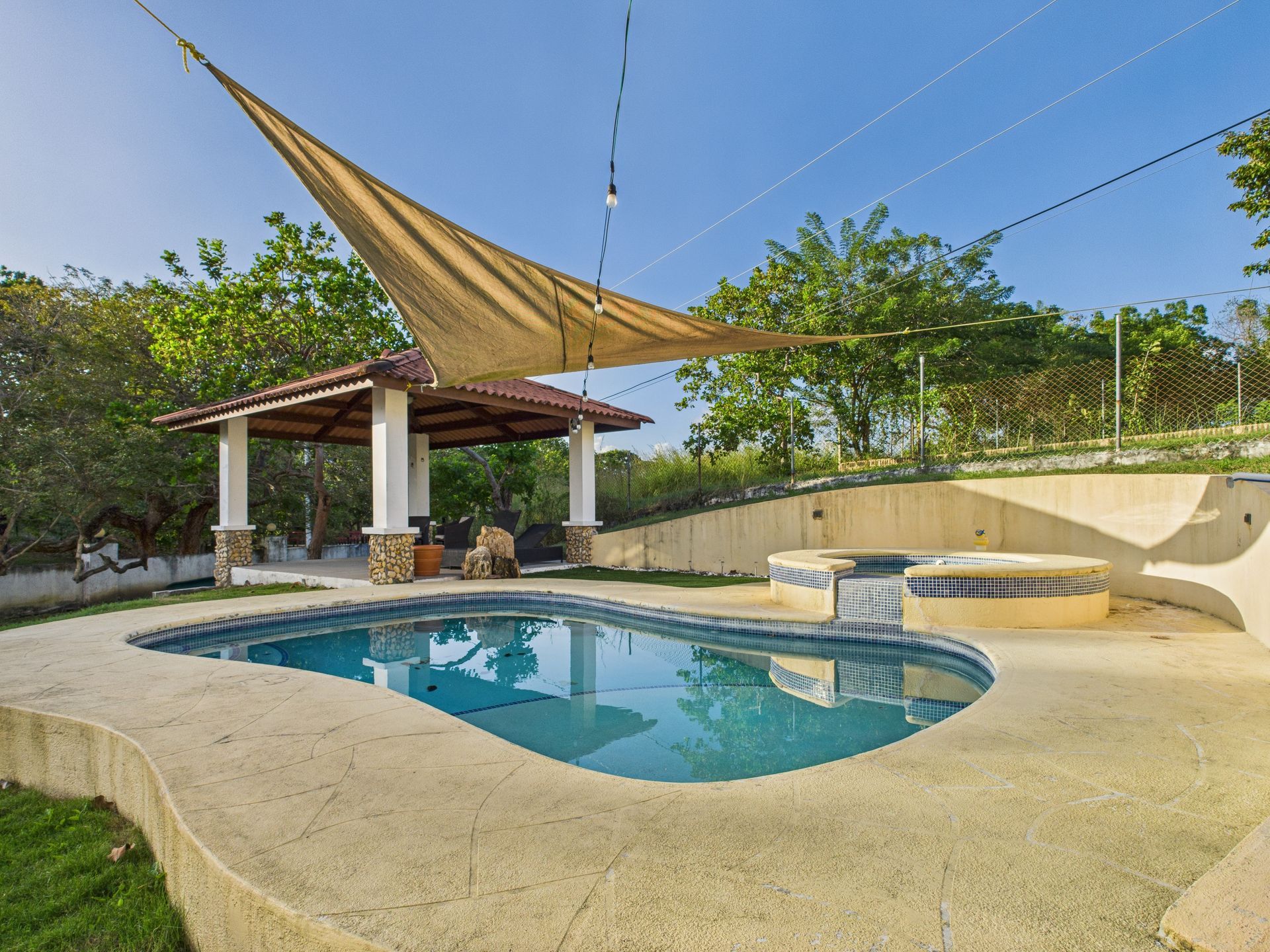 Piscina con cenador y sombrilla bajo un cielo azul.