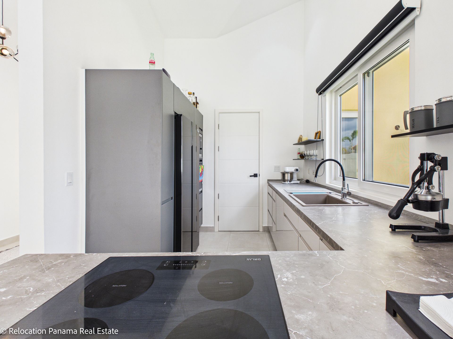 Cocina moderna con refrigerador gris, encimera con diseño de piedra, placa de cocina negra y puerta blanca.