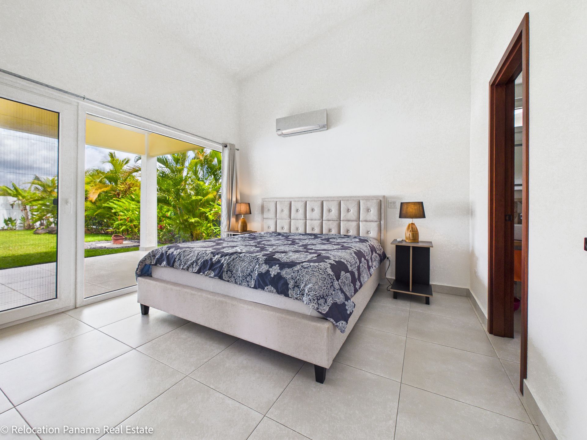 Dormitorio moderno con cama, ropa de cama con estampado azul, mesita de noche con lámpara, aire acondicionado y puertas corredizas de cristal que dan al patio.