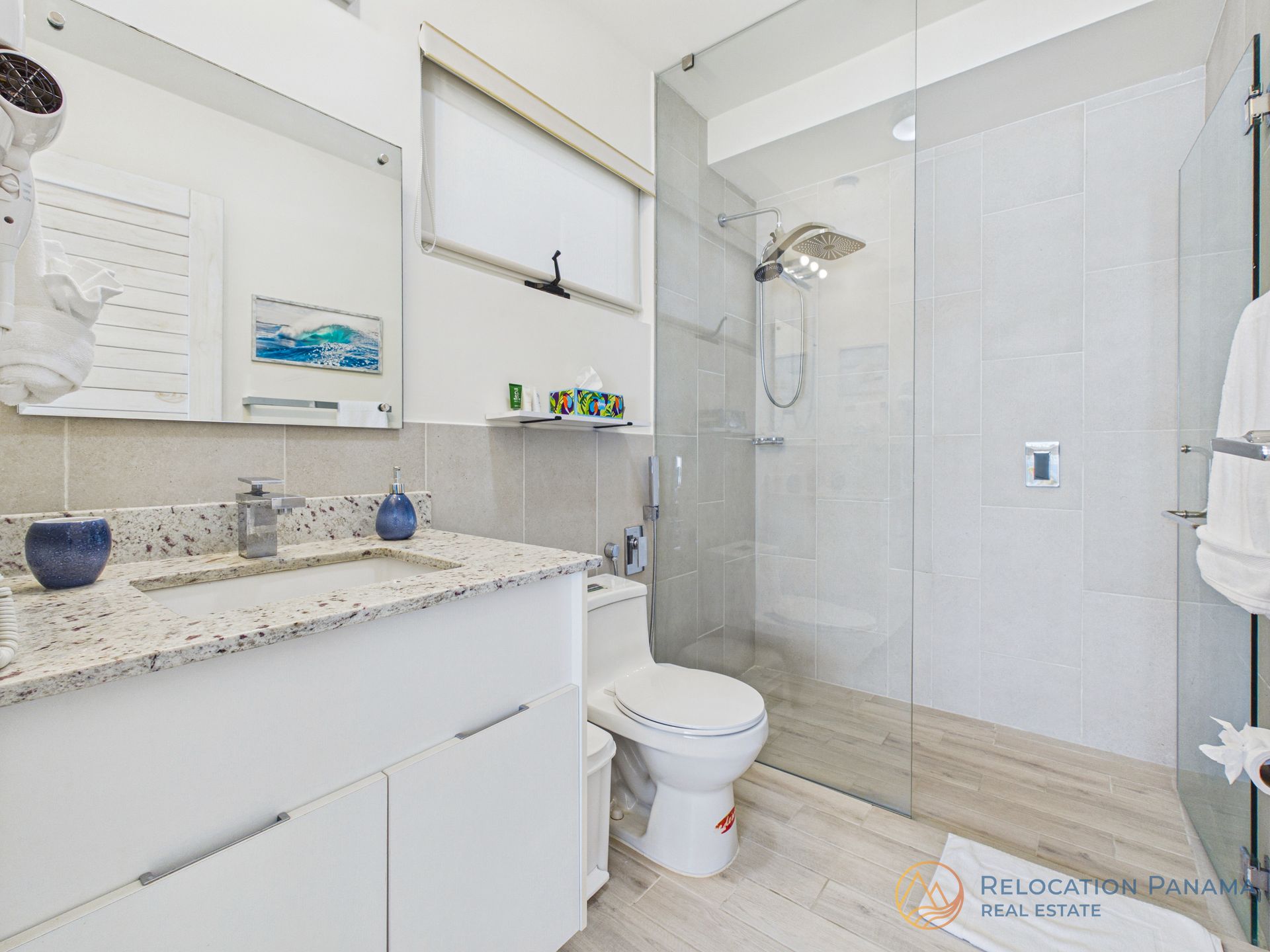 Un baño moderno con tocador blanco con encimera moteada, inodoro y ducha a ras de suelo con mampara de cristal.