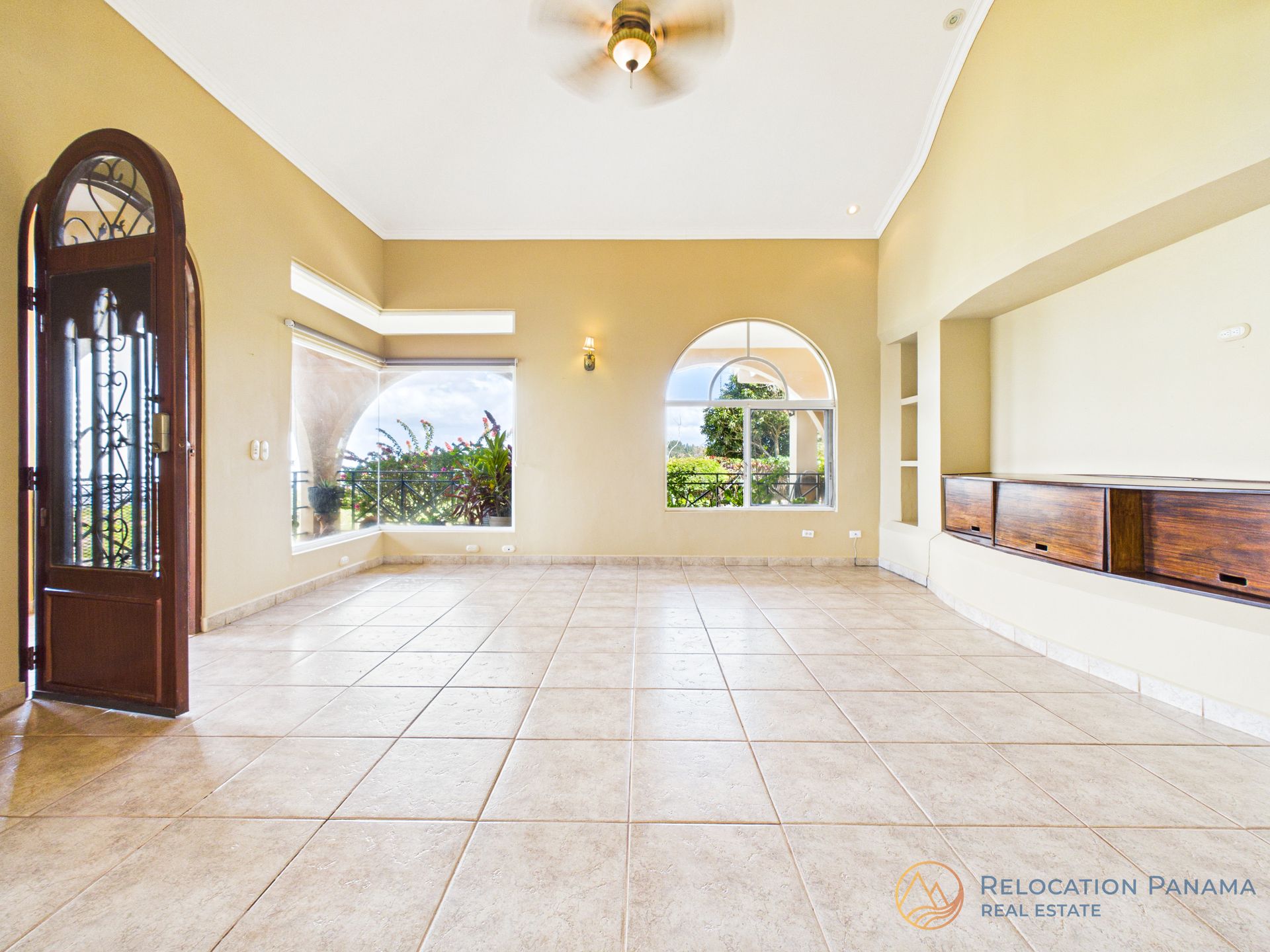 Una habitación espaciosa con paredes color crema, suelos de baldosas, techos abovedados, ventanas arqueadas y un armario empotrado de madera.