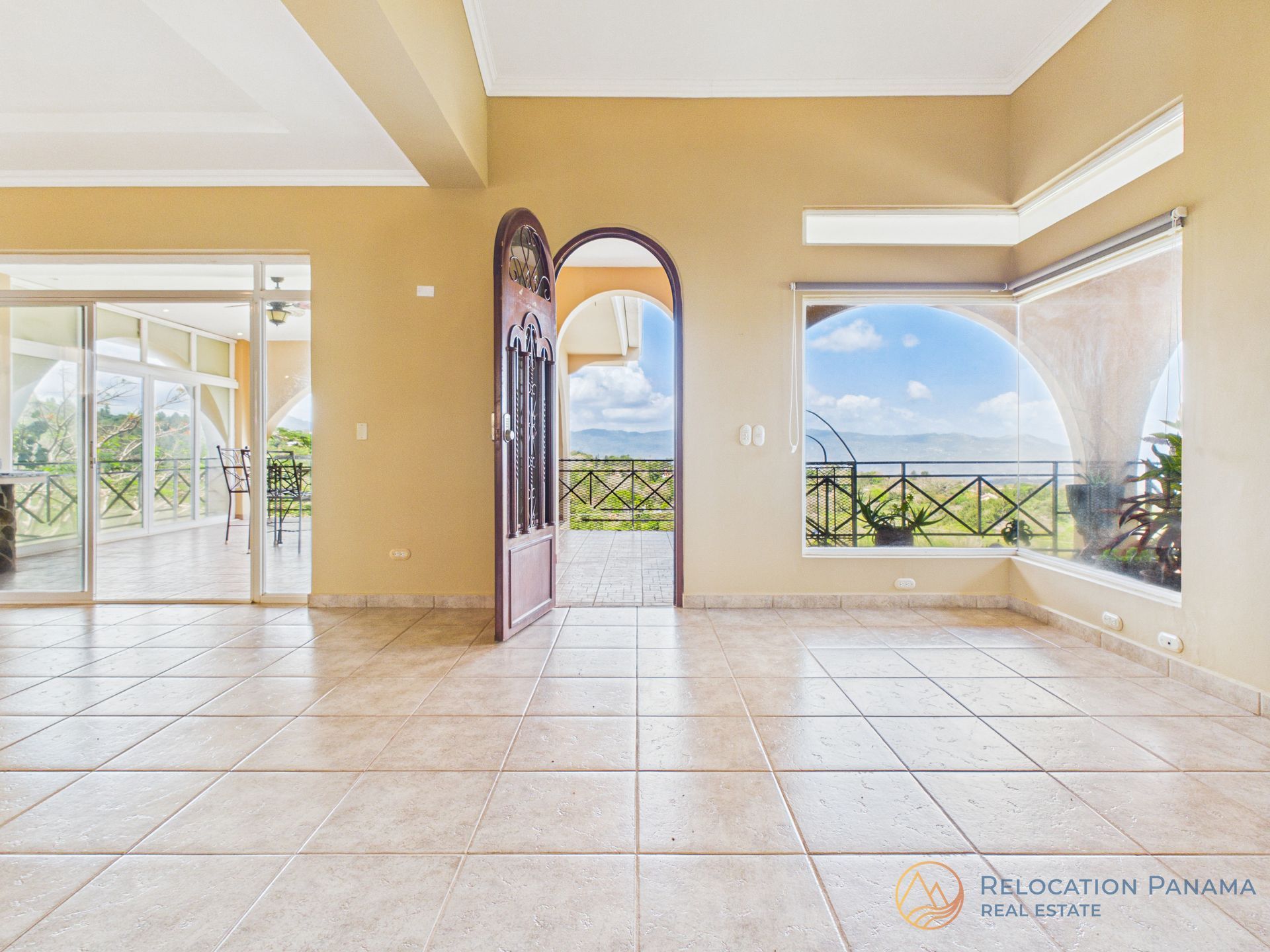 Una habitación vacía con paredes de color beige y suelos de baldosas, con una puerta abierta y grandes ventanales con vistas a un paisaje pintoresco.