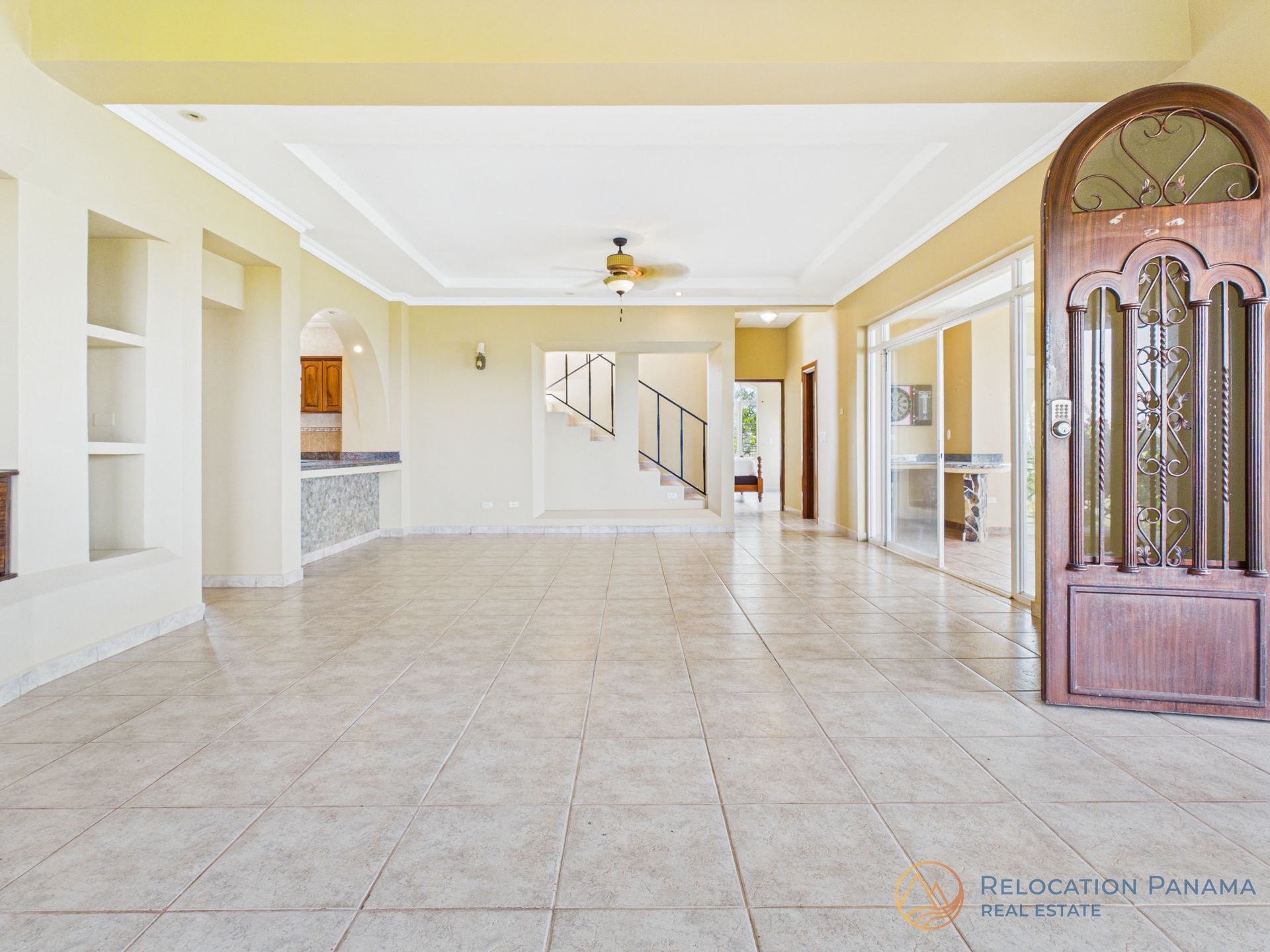 Interior espacioso con suelos de baldosas, una puerta de madera tallada, estanterías empotradas en la pared y vistas a una escalera abierta.