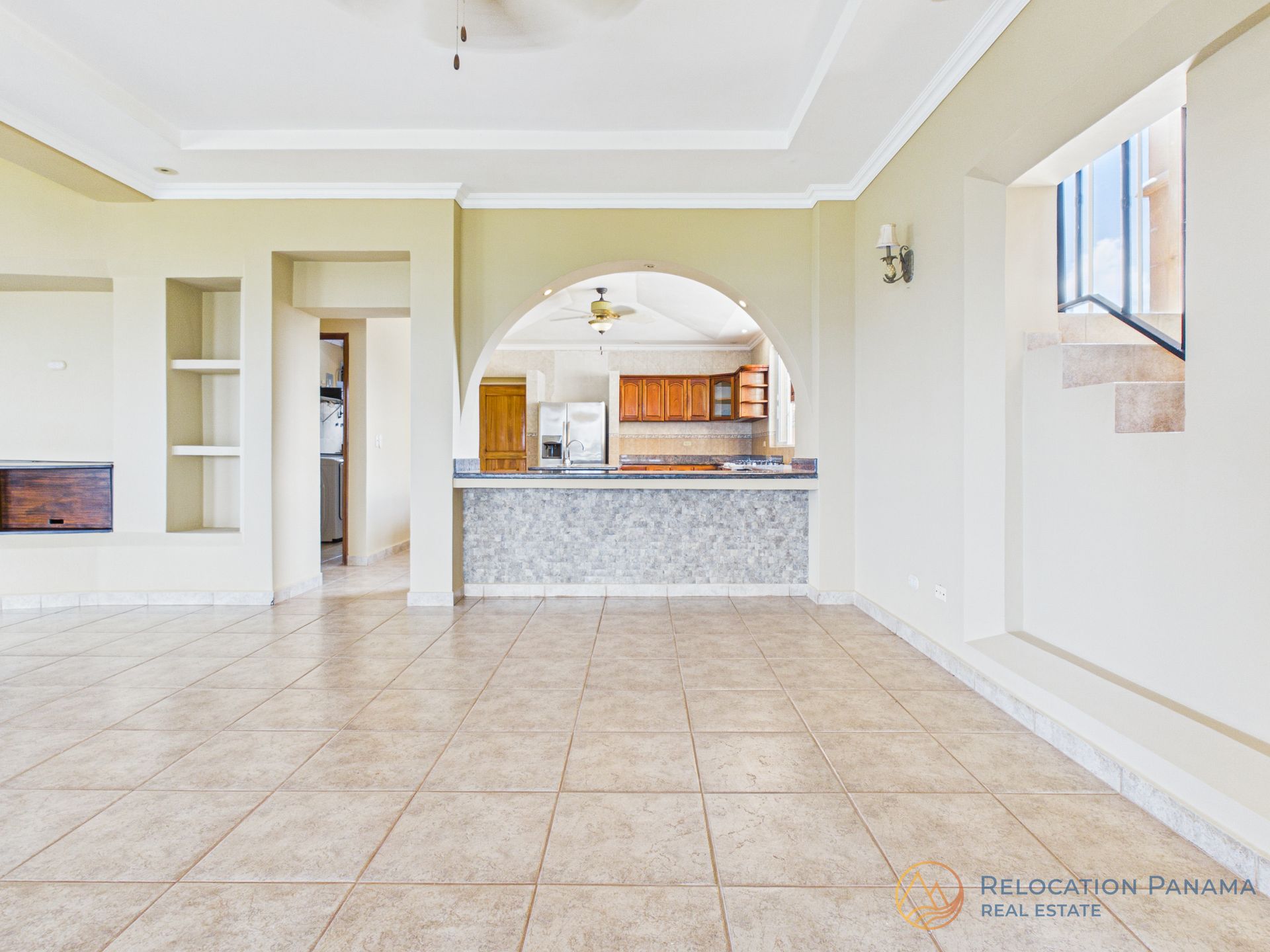 Una habitación amplia y diáfana con suelo de baldosas beige, chimenea y una barra de desayuno que la separa de la cocina.
