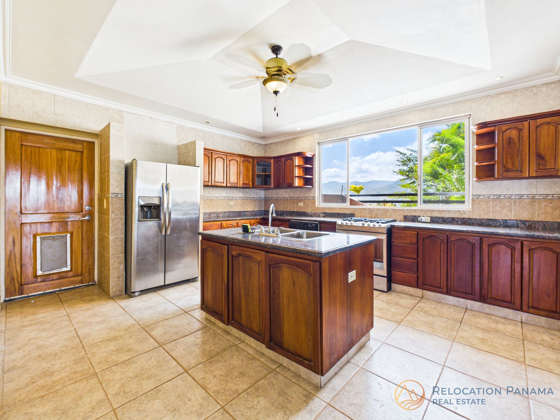 Una cocina espaciosa con armarios de madera, una isla central, nevera de acero inoxidable y una gran ventana con vistas.