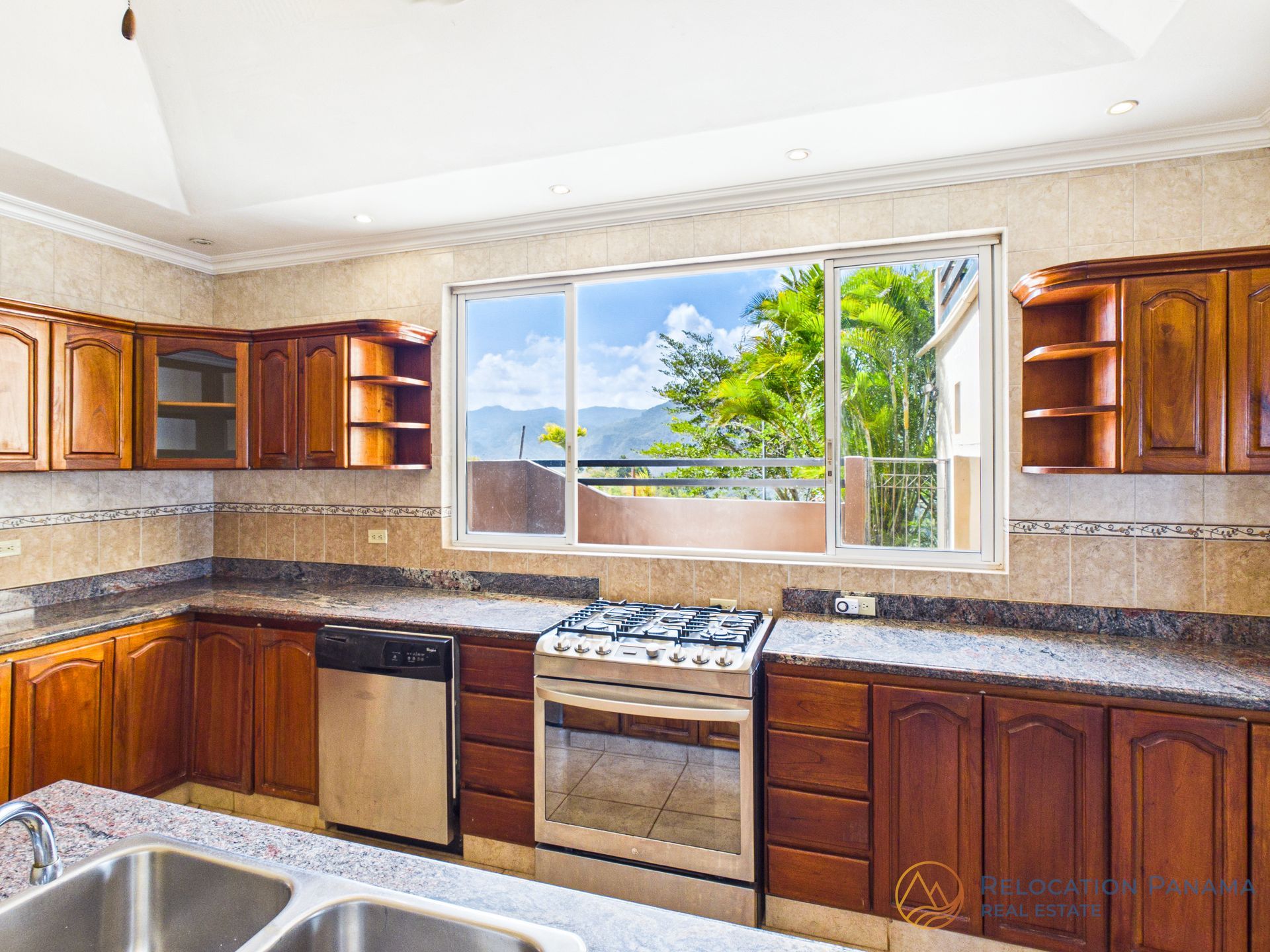 Una cocina moderna con armarios de madera, una estufa de acero inoxidable y una ventana con vistas a la montaña y a la vegetación.