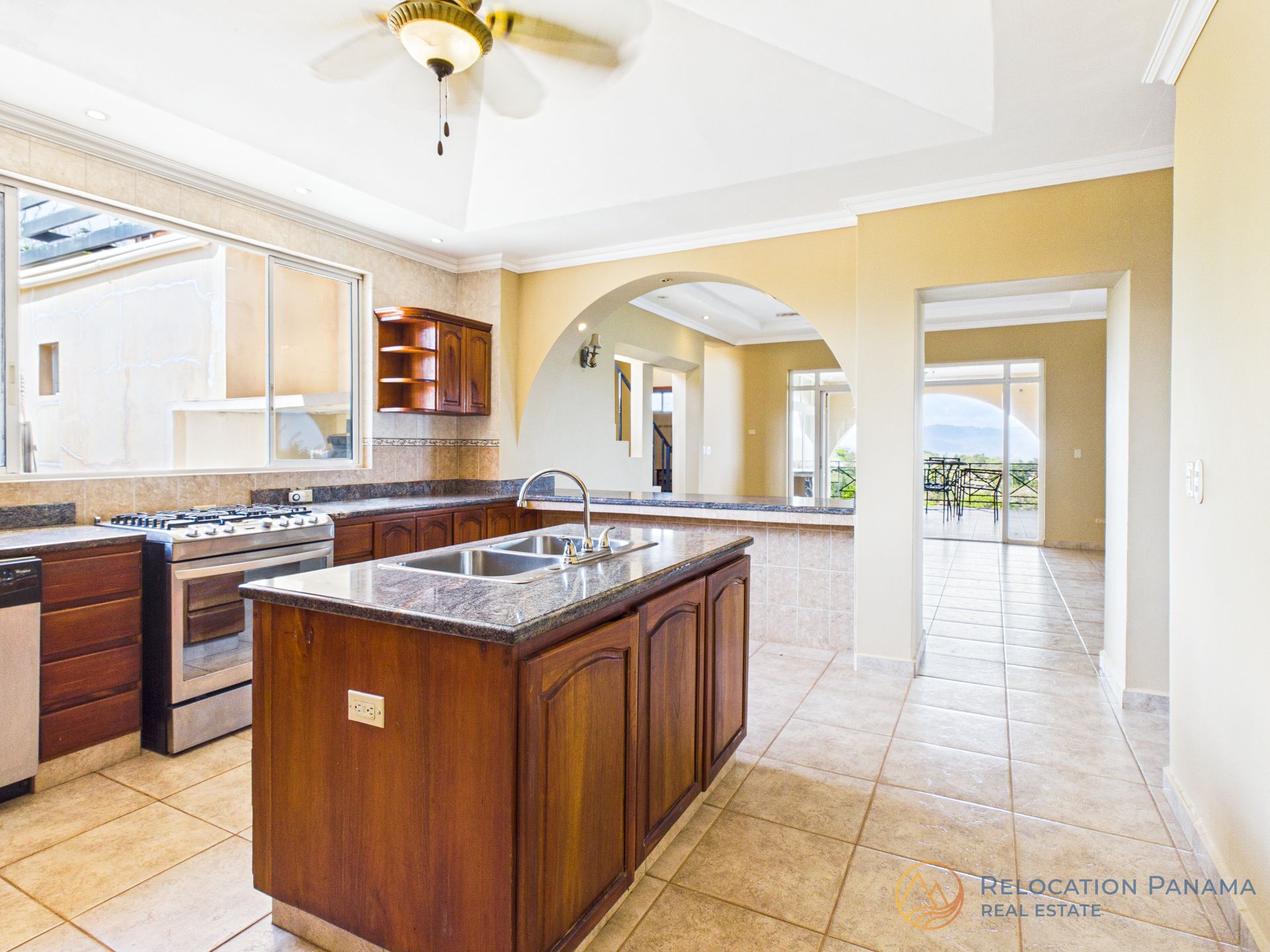 Amplia cocina con armarios de madera, encimeras de piedra, isla central, electrodomésticos de acero inoxidable y suelos de baldosas beige.