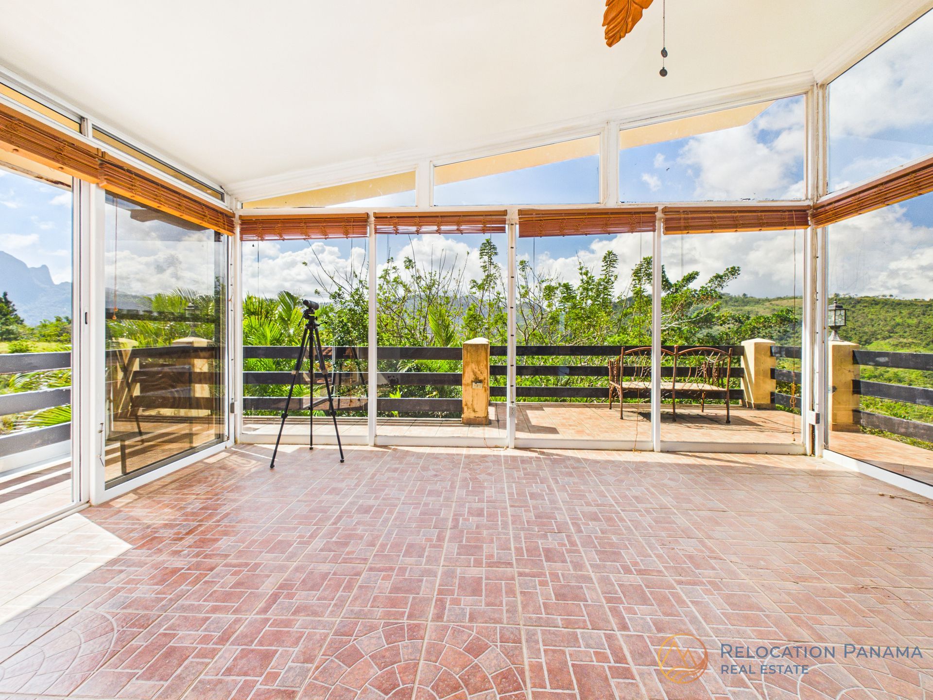 Una terraza acristalada con suelo de ladrillo rojo, paredes de cristal y vistas a un exuberante paisaje verde y a las montañas lejanas.