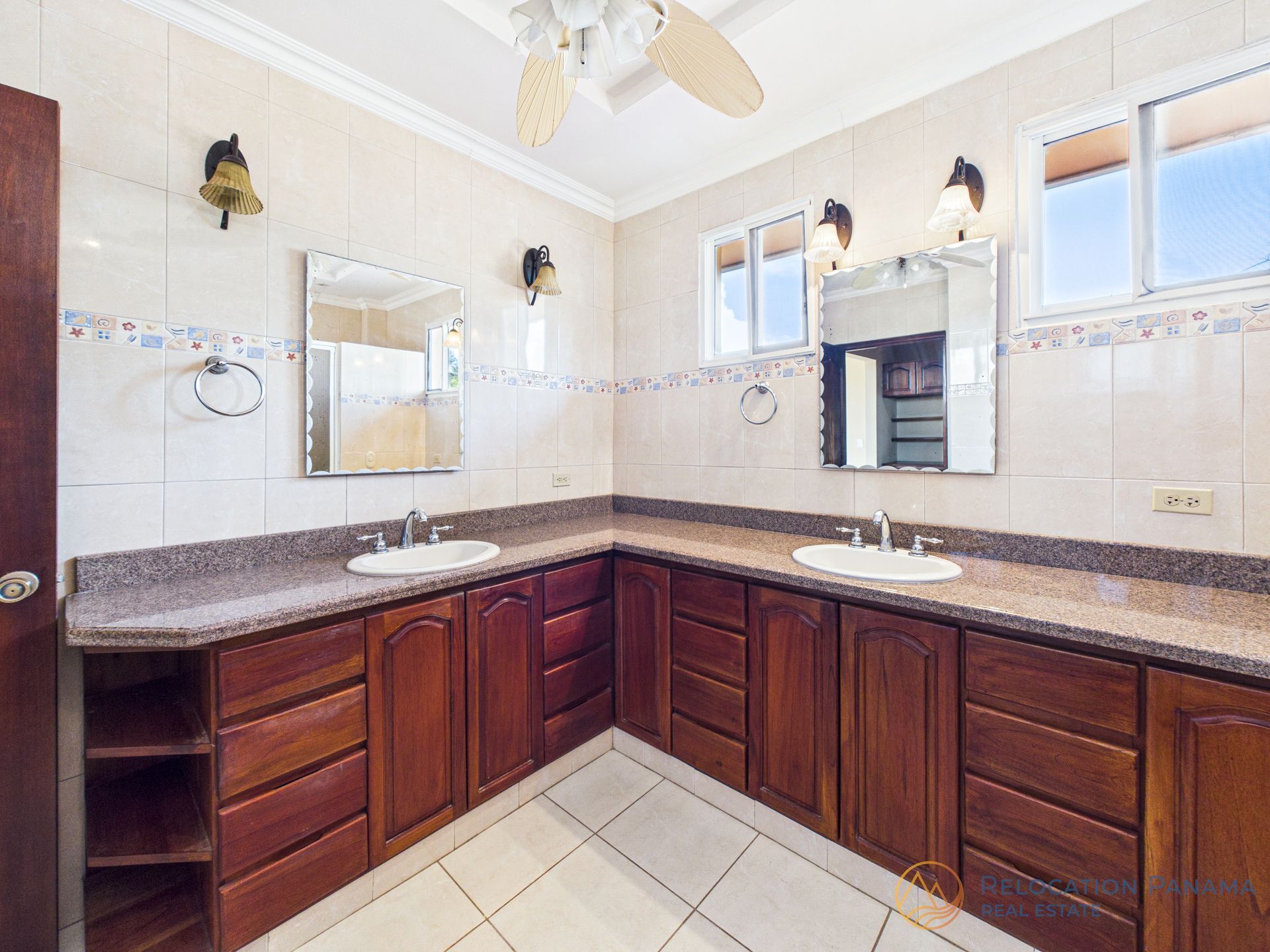 Un baño espacioso con dos lavabos, armarios de madera oscura, encimera de granito y paredes alicatadas en tonos claros.