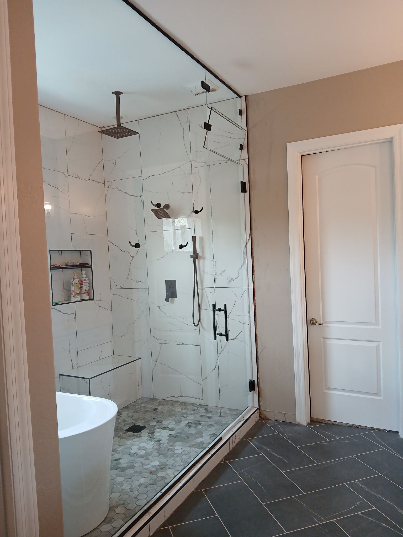 Modern bathroom with glass shower, white tile, freestanding tub, and dark herringbone floor