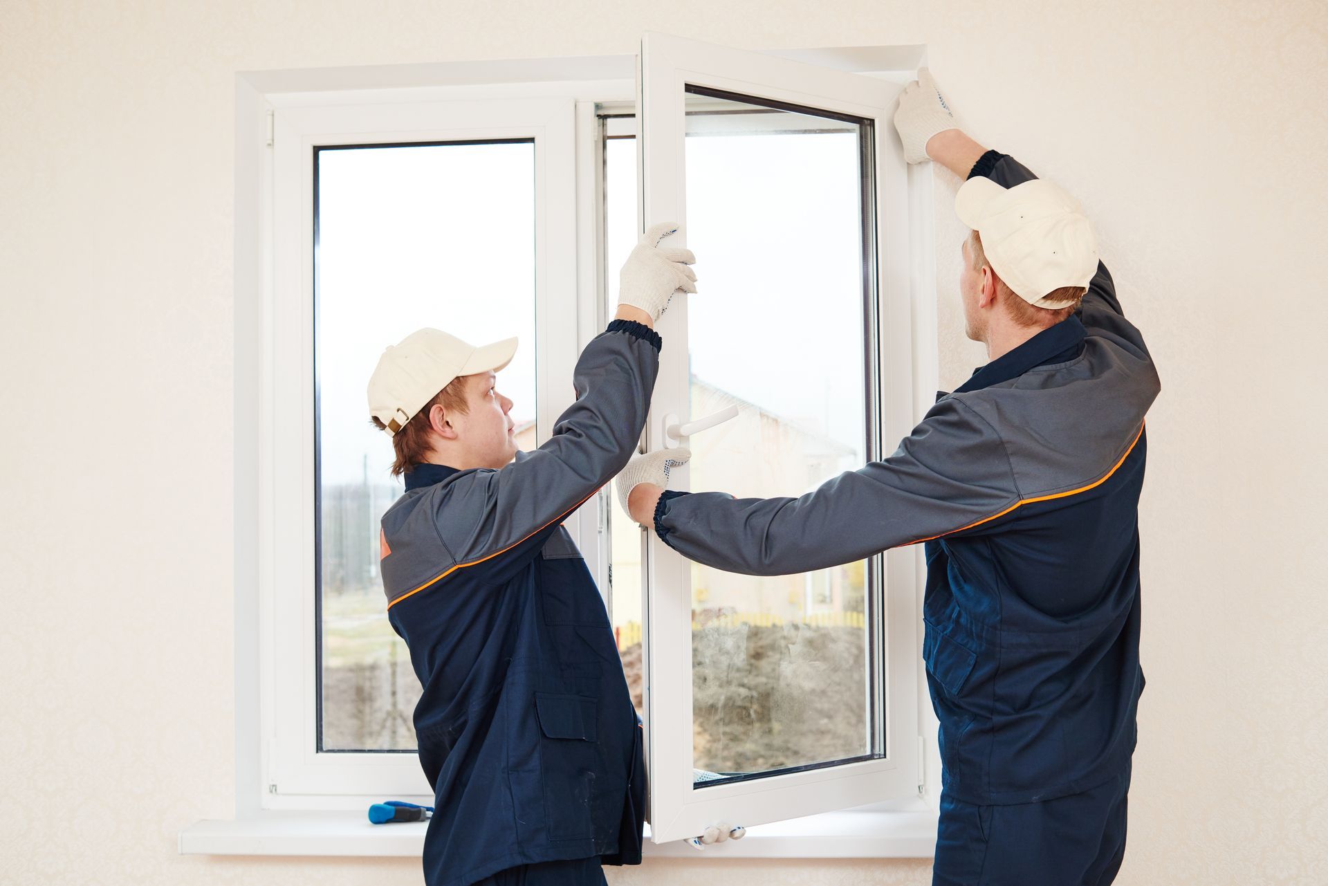 Two workers installing a white window frame in a bright room