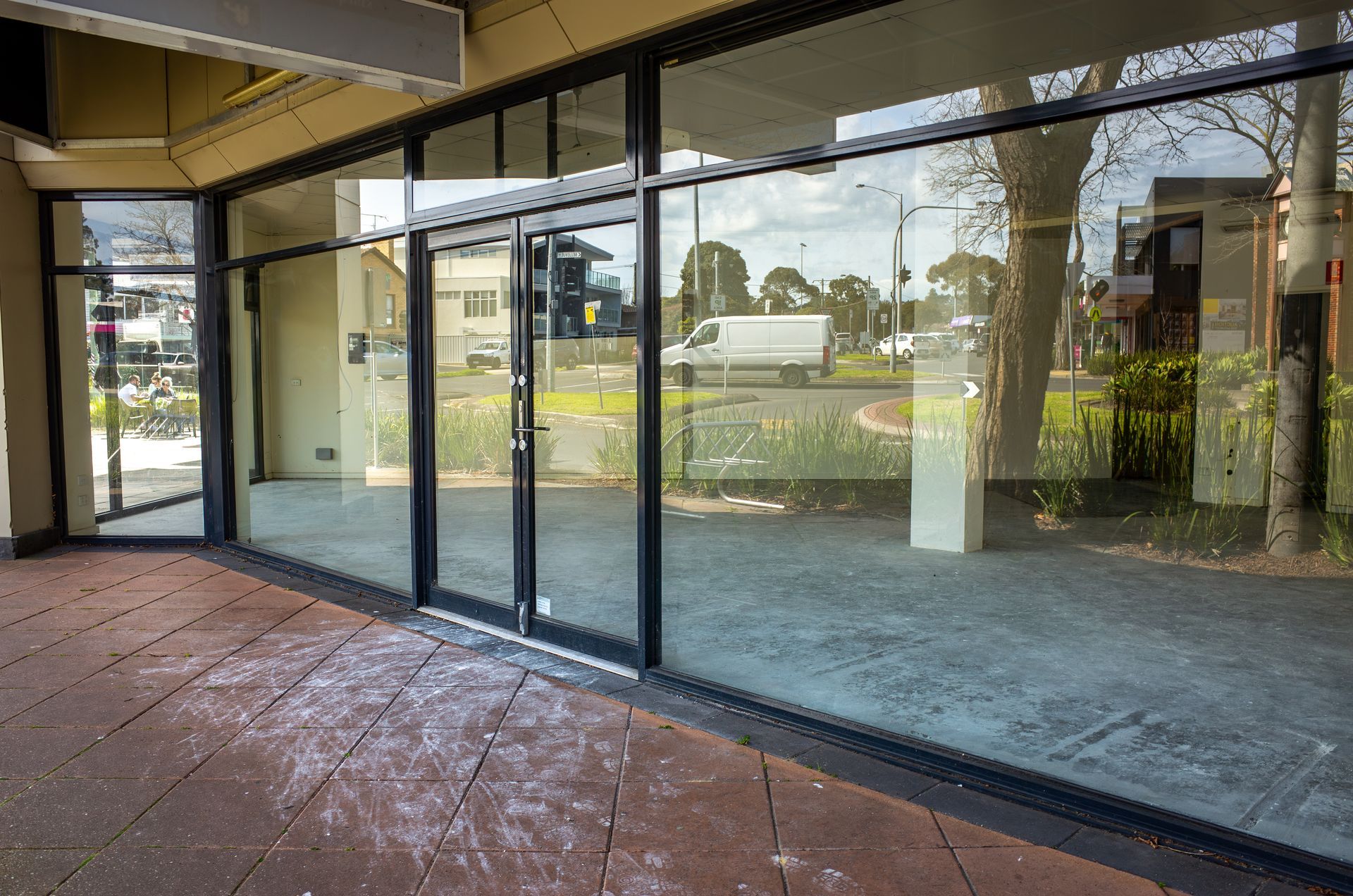Empty storefront with large glass windows and red tiled walkway reflected outside