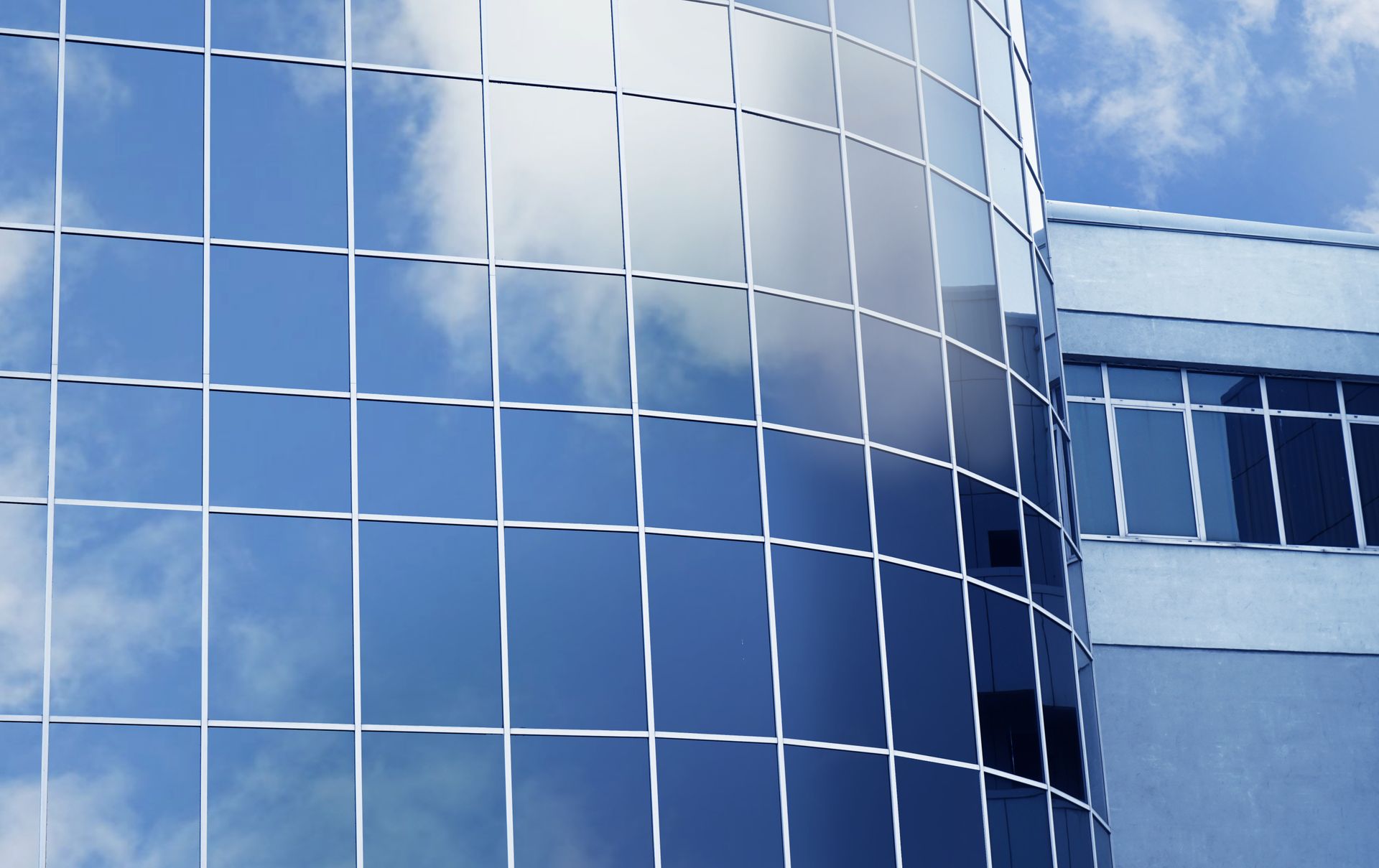 Blue glass office building facade with curved reflective windows and white grid lines