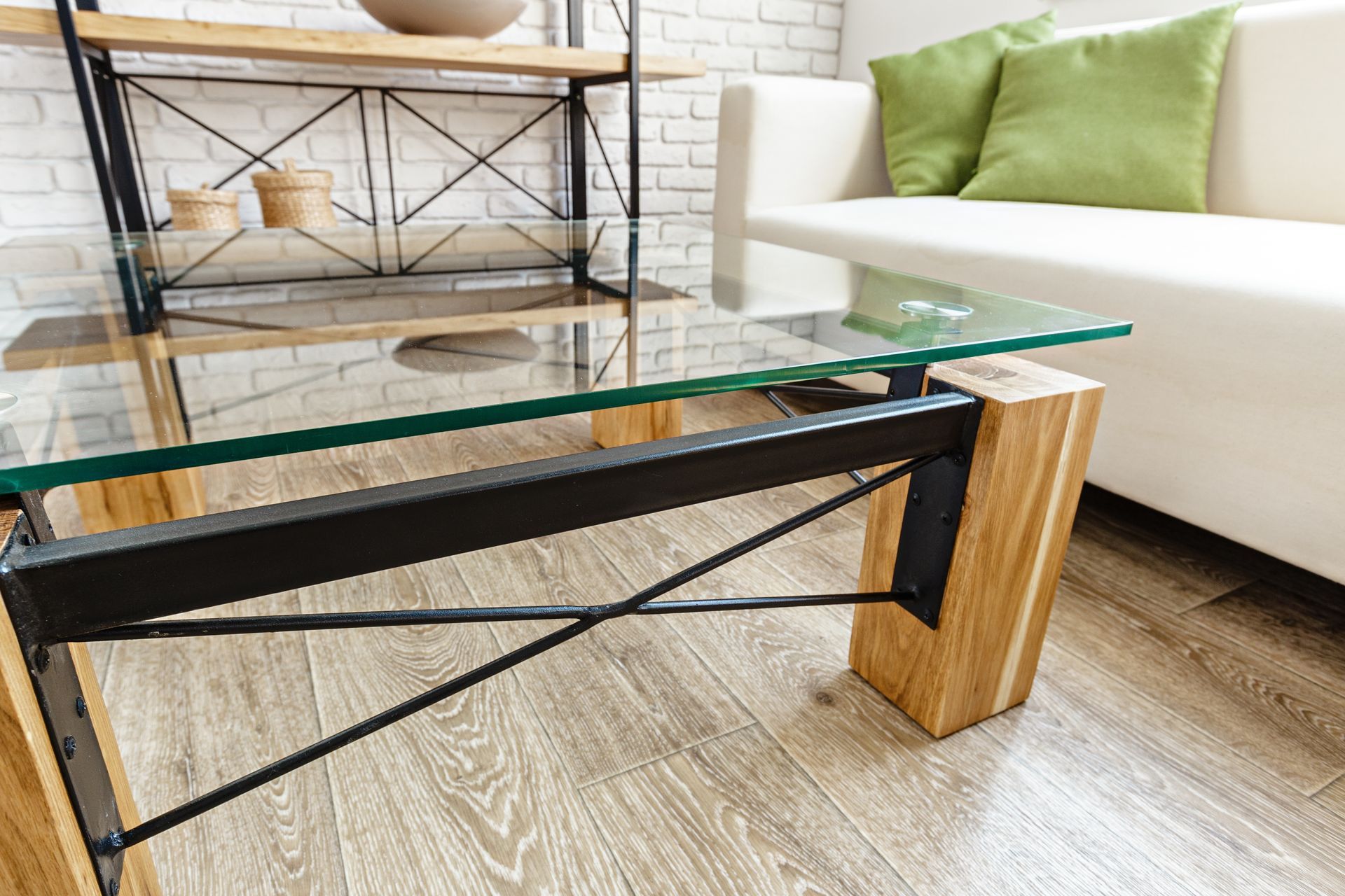 Glass coffee table with black metal frame and wood supports in a bright living room.