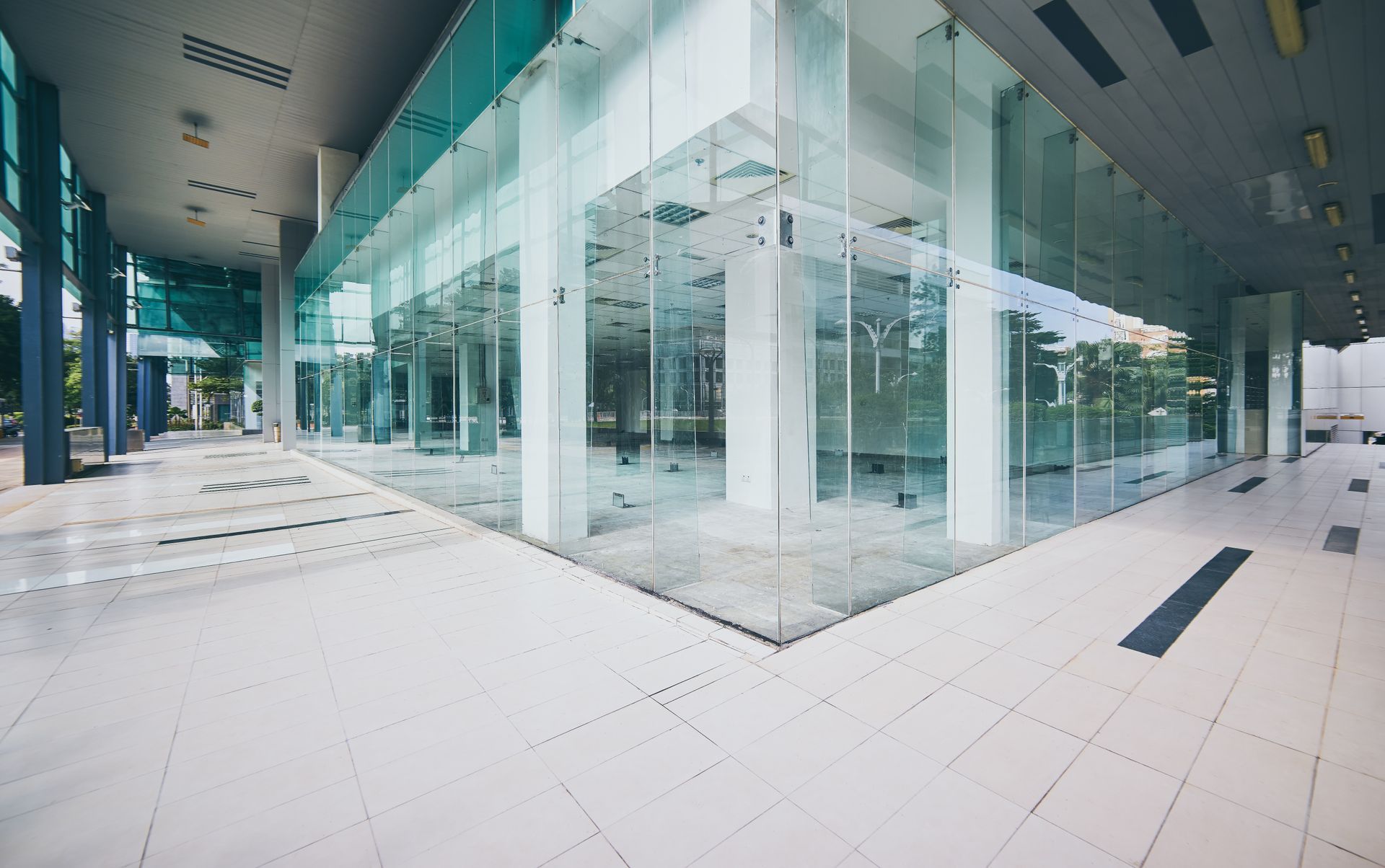 Modern glass office lobby with white tile floors and teal accents, empty and brightly lit