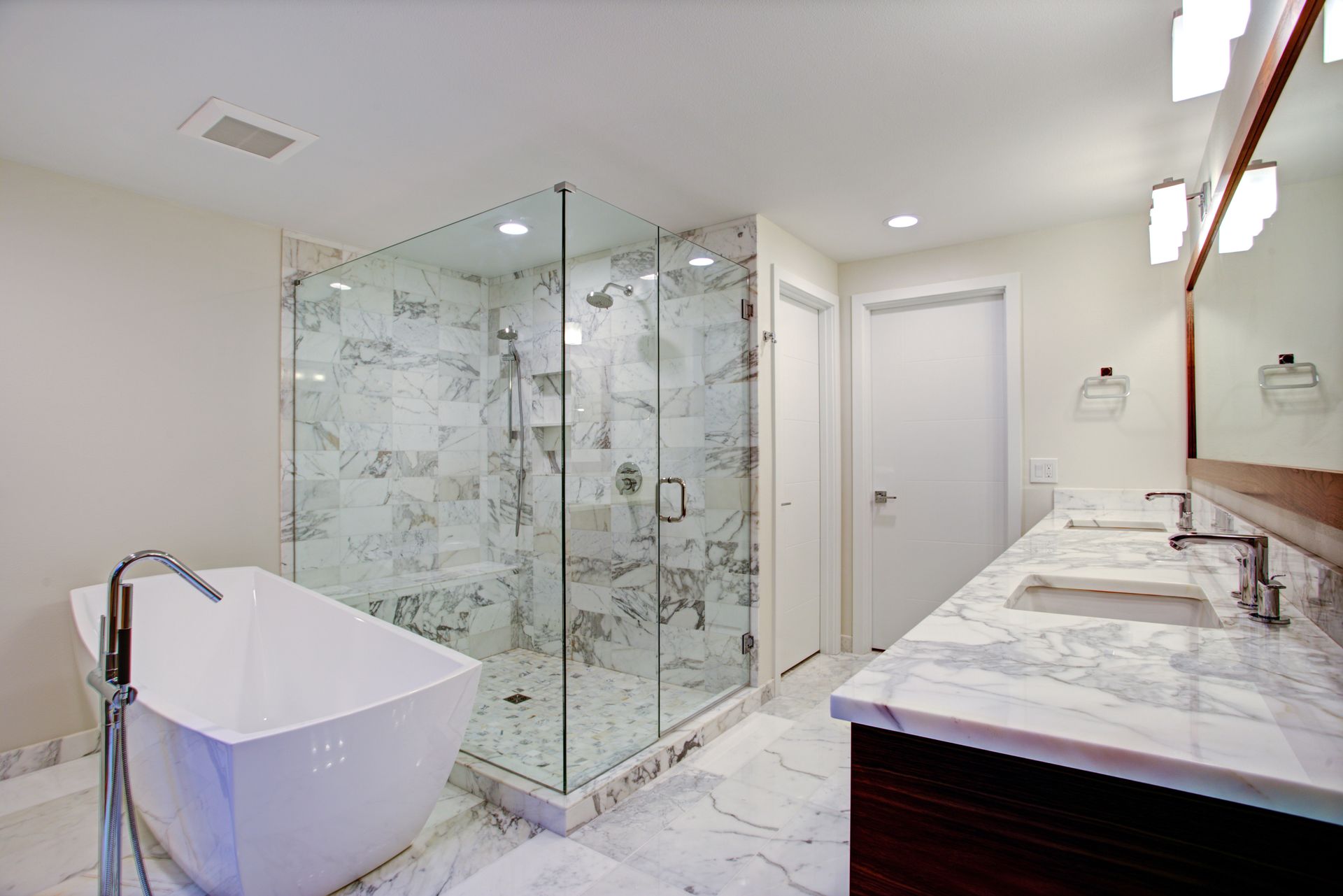 Modern white bathroom with glass-enclosed shower, freestanding tub, and marble vanity