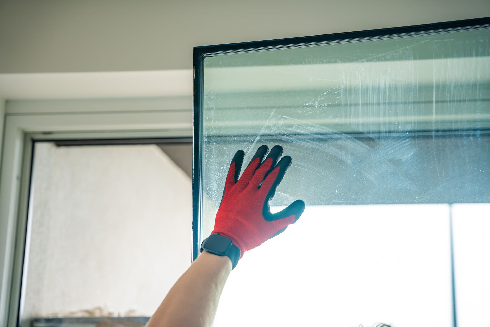 Gloved hand cleaning a glass window pane inside a room