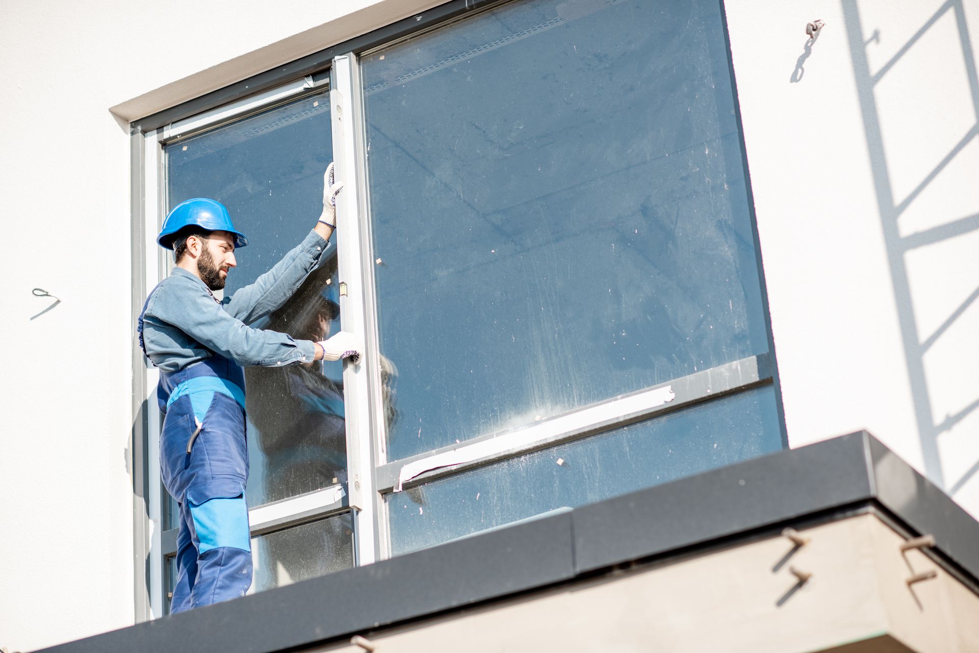 Worker in blue uniform and hard hat adjusting a large window on a building exterior