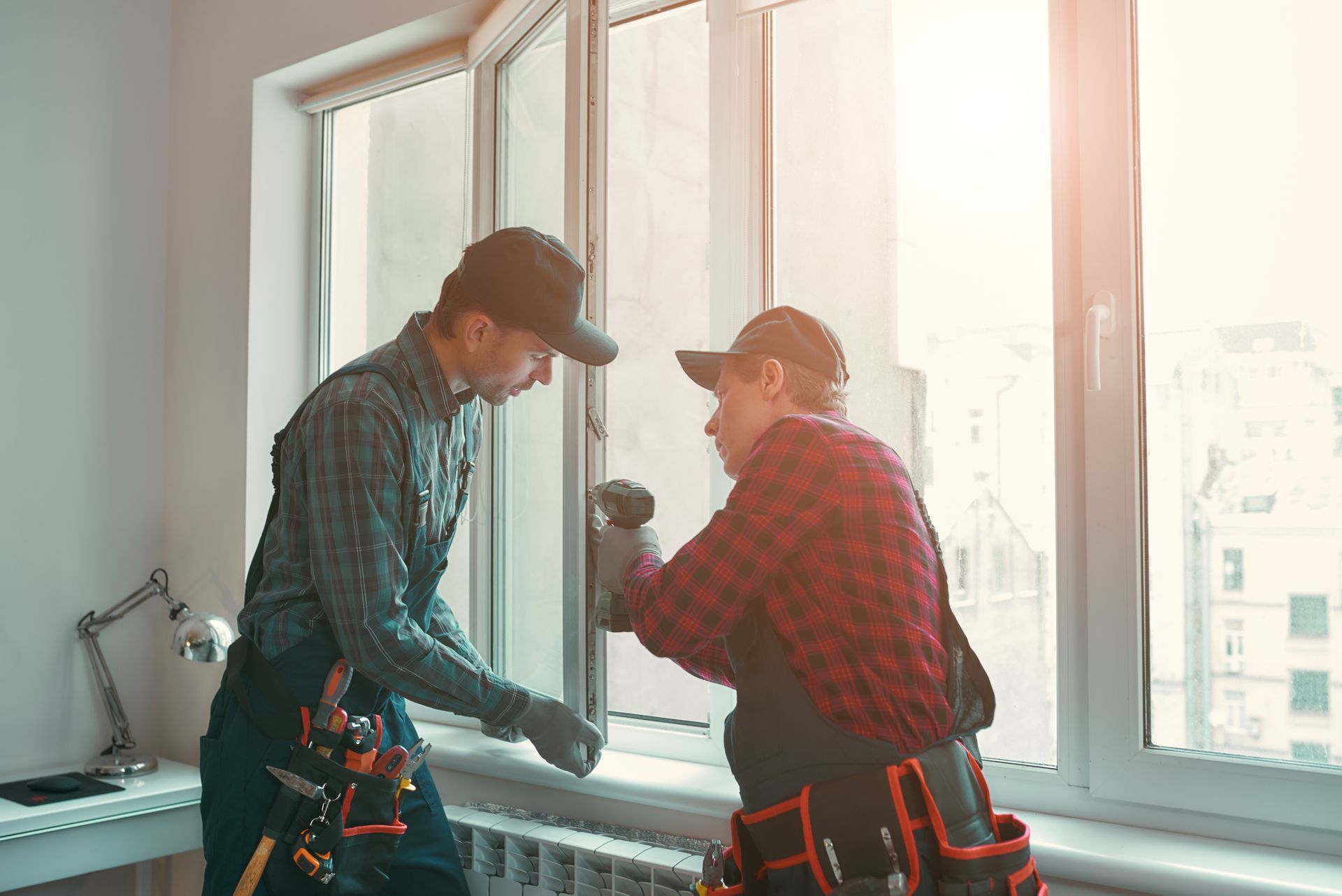 Two workers in safety gear repair a window inside a bright room