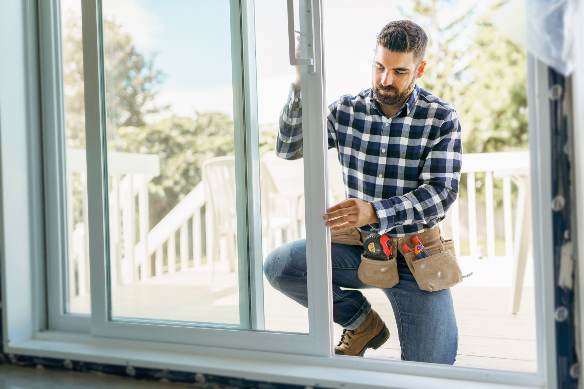Worker installing a window pane indoors, holding a toolbox near a large glass window