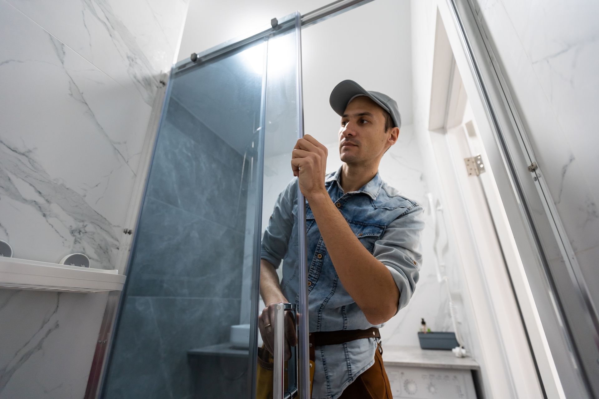 Worker installing a glass shower door in a bathroom, holding the metal frame.