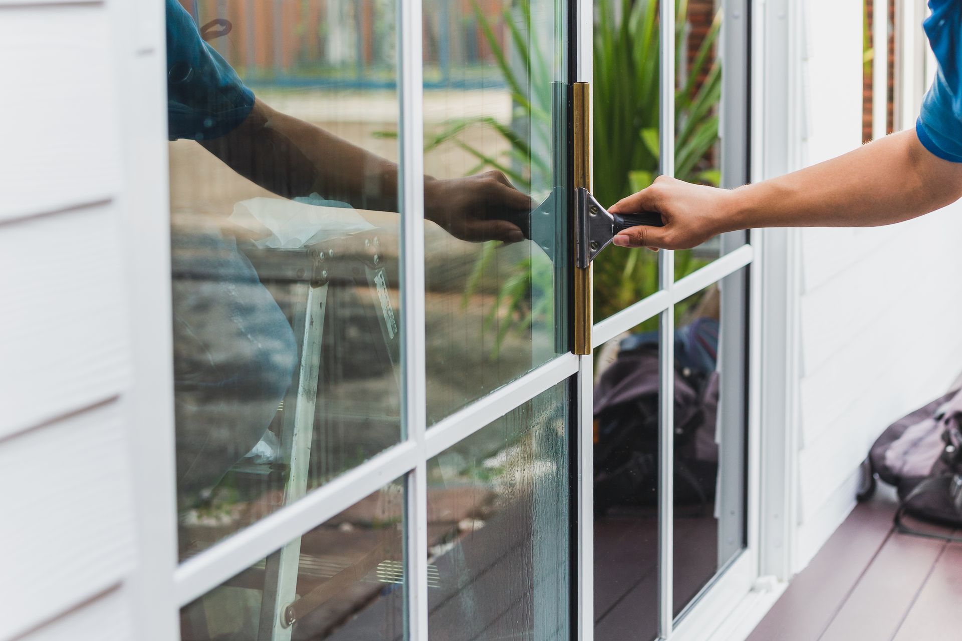 Person opening a glass patio door with a black handle on a white porch