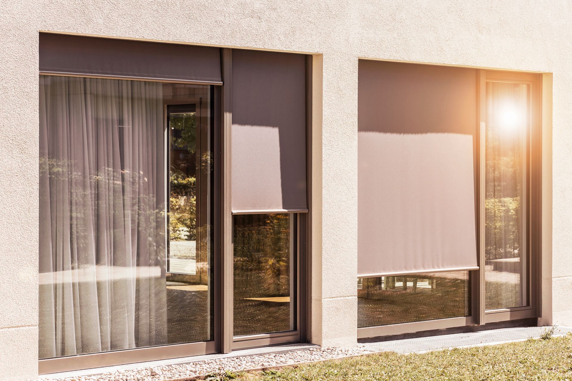 Modern house exterior with two large windows, curtains, and sunlight shining in from the right.