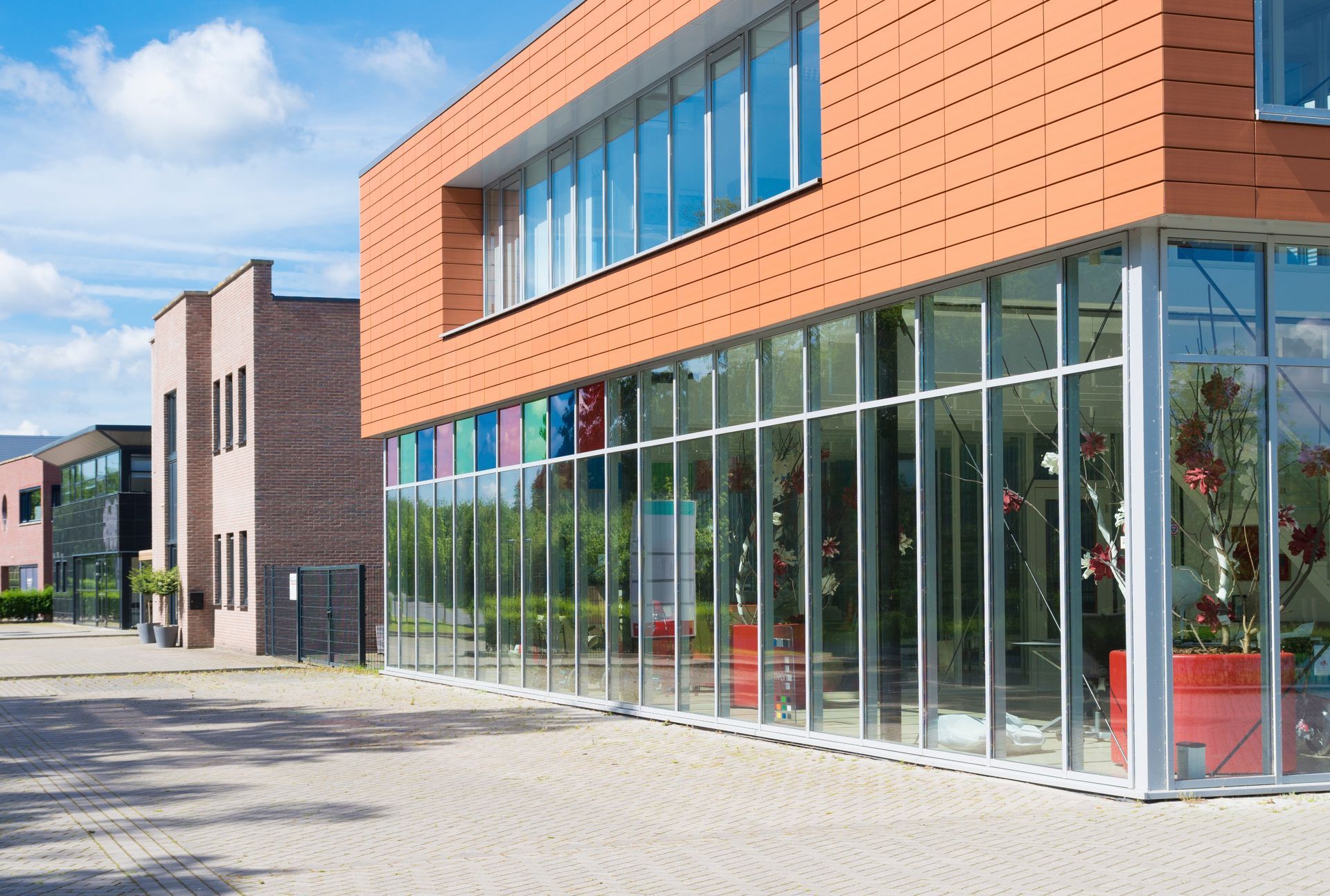 Modern building with orange brick, large glass storefront windows, and a paved sidewalk outside