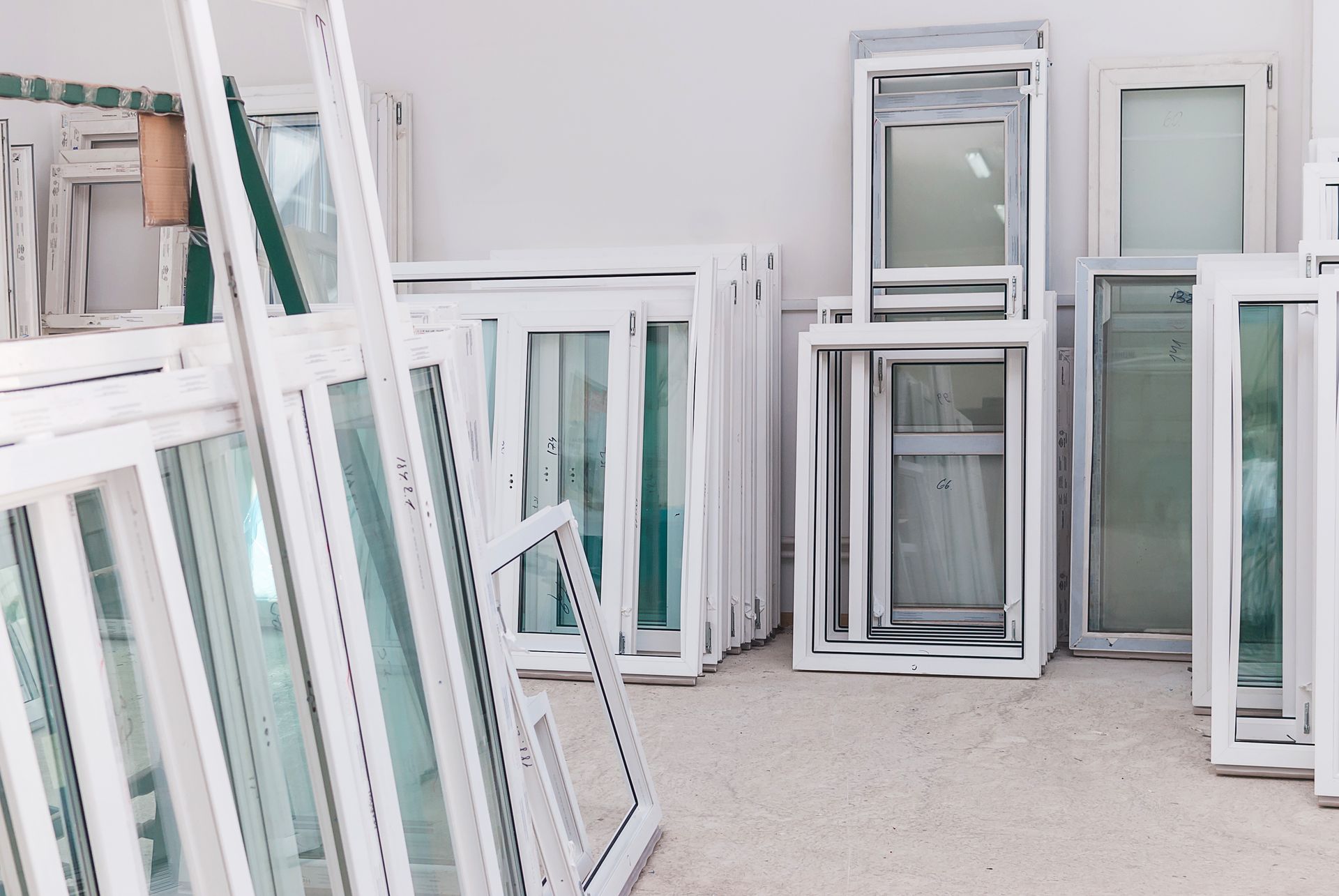Stacked white window frames and doors in a bright workshop or storage space